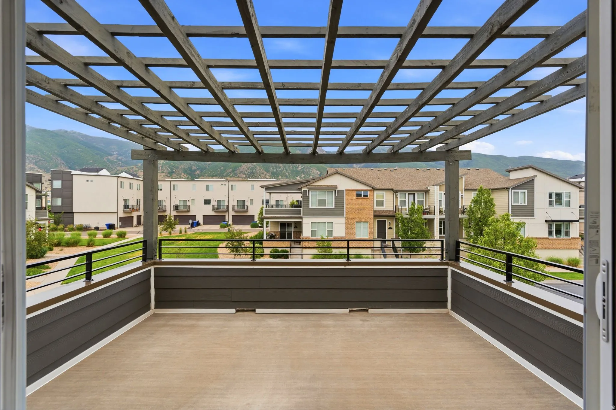 Expansive outdoor deck featuring a slat pergola, concrete-style flooring, dark siding, and black metal railings