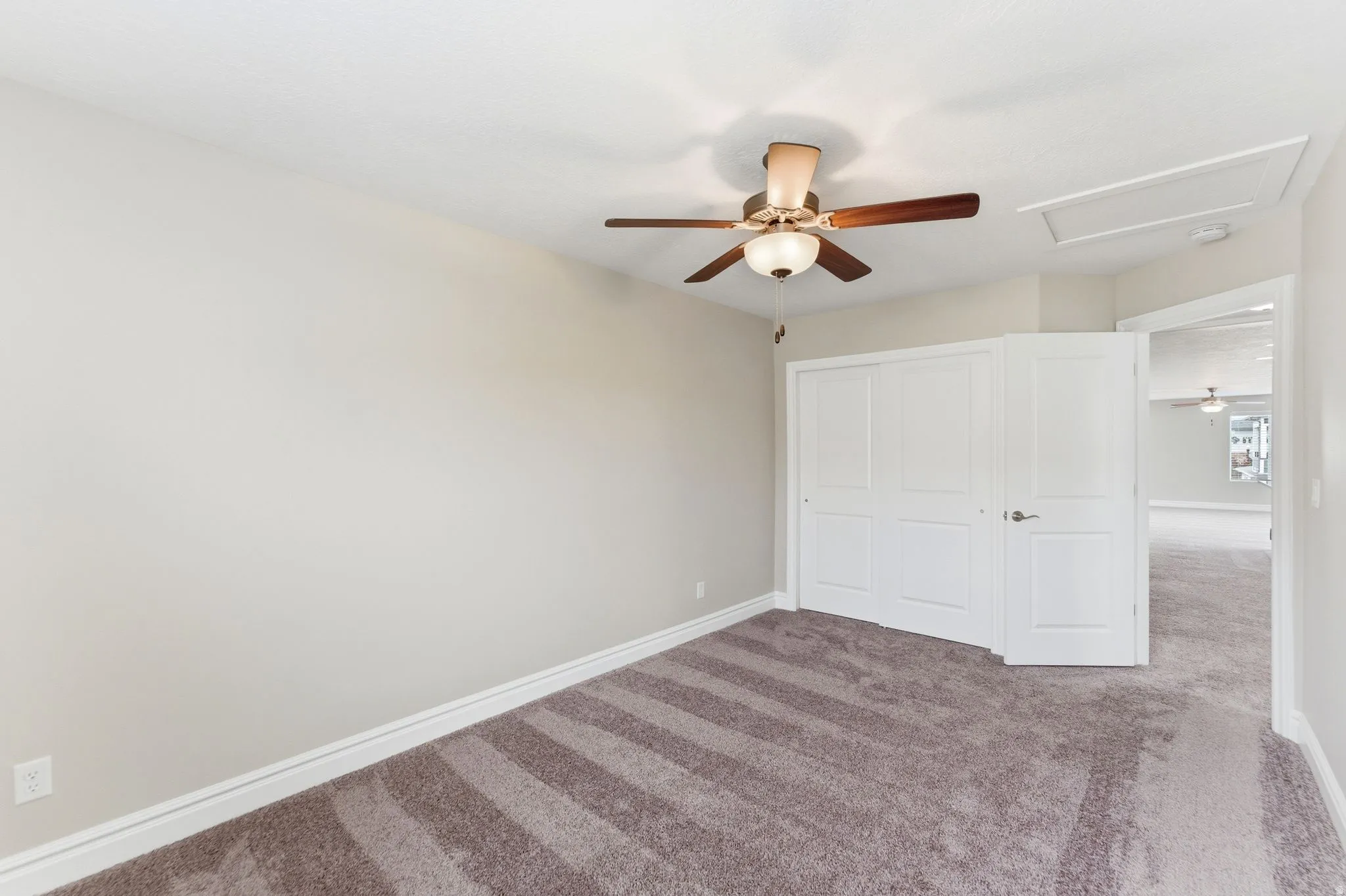 Carpeted room featuring a ceiling fan with integrated lighting, white baseboards, a built-in closet with bi-fold doors, and a paneled door