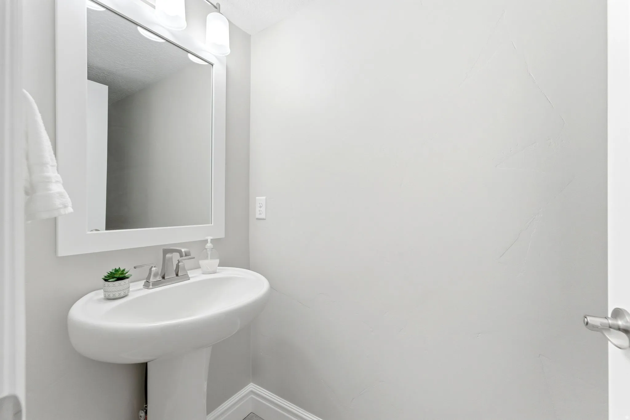 Pedestal sink with chrome faucet, framed mirror, and wall-mounted light fixture