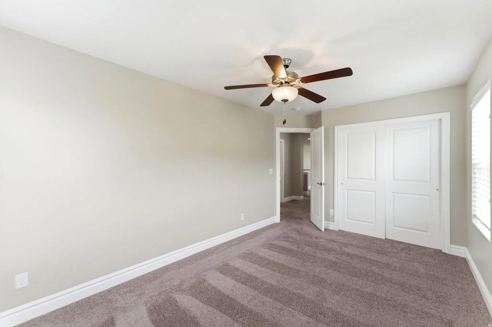 Bedroom featuring plush carpet flooring, a ceiling fan with integrated lighting, white baseboards, and a double-door closet with panel detailing