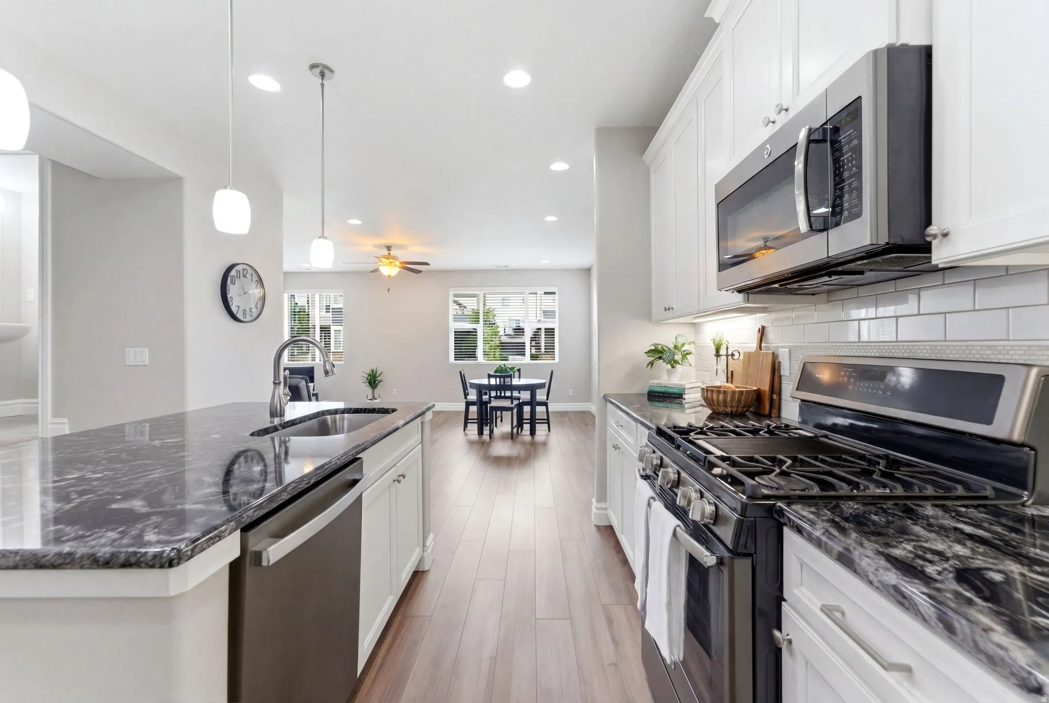 Modern kitchen featuring dark granite countertops, white cabinetry, stainless steel appliances, and wood-finish flooring