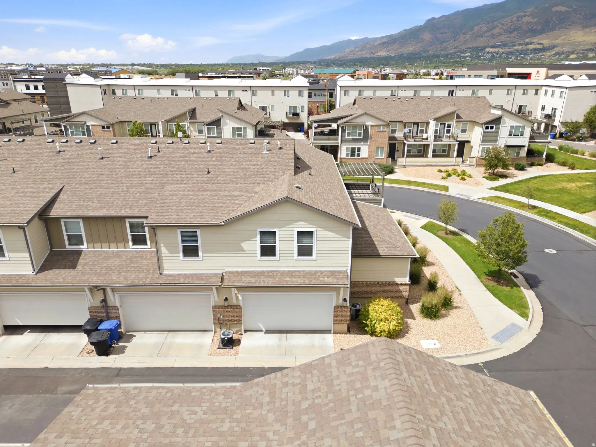 Townhome exterior featuring tan siding, a brown shingled roof, and a two-car garage