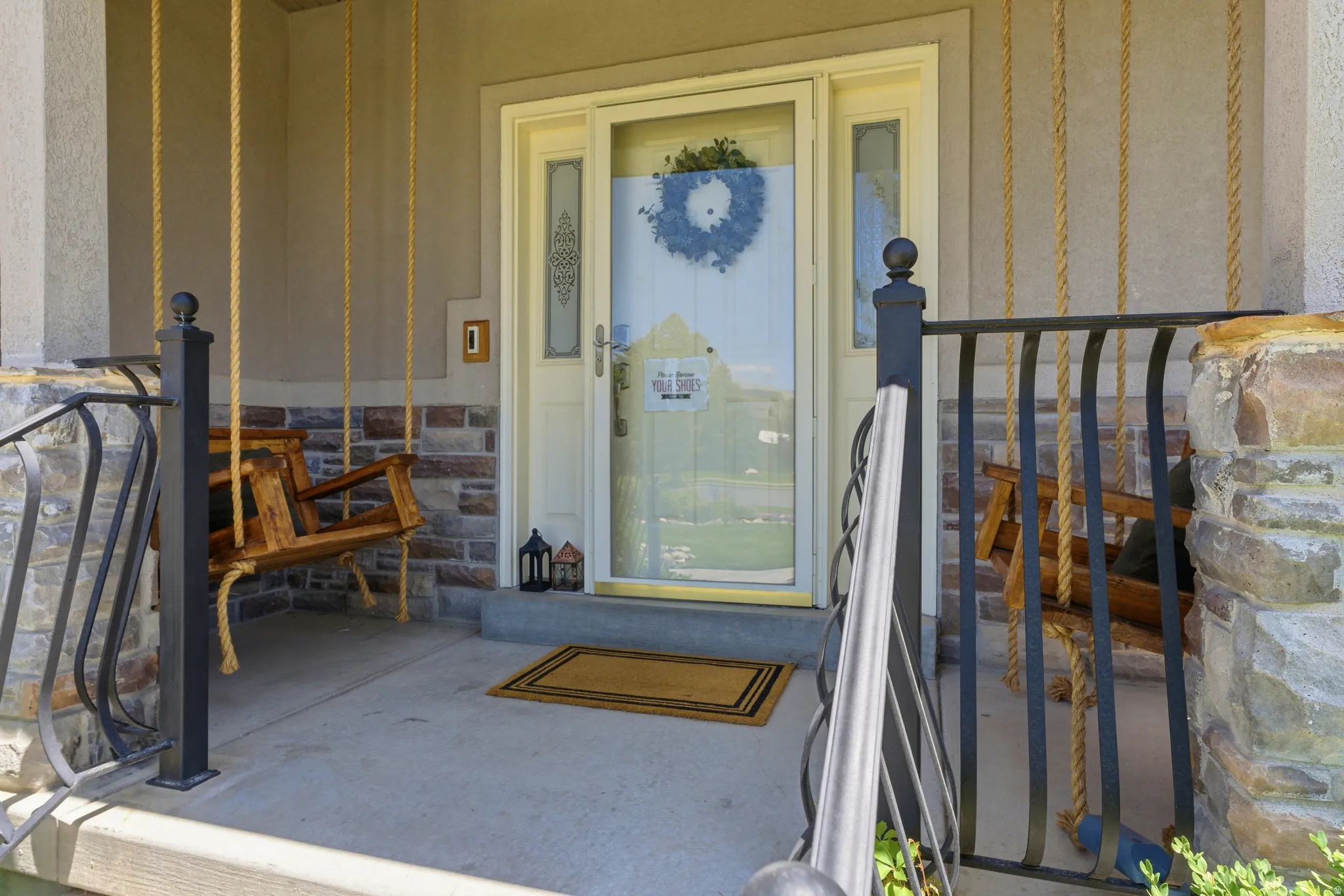 Covered front porch featuring a stone facade accent, concrete flooring, and decorative metal railings