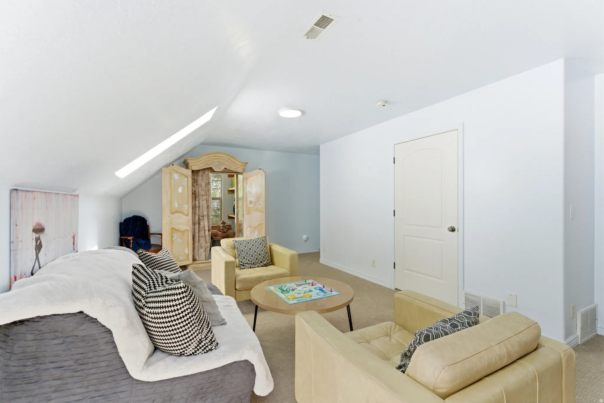 Spacious attic room featuring a vaulted ceiling with a skylight, light-colored carpeting, a neutral wall color, and a cream-painted door