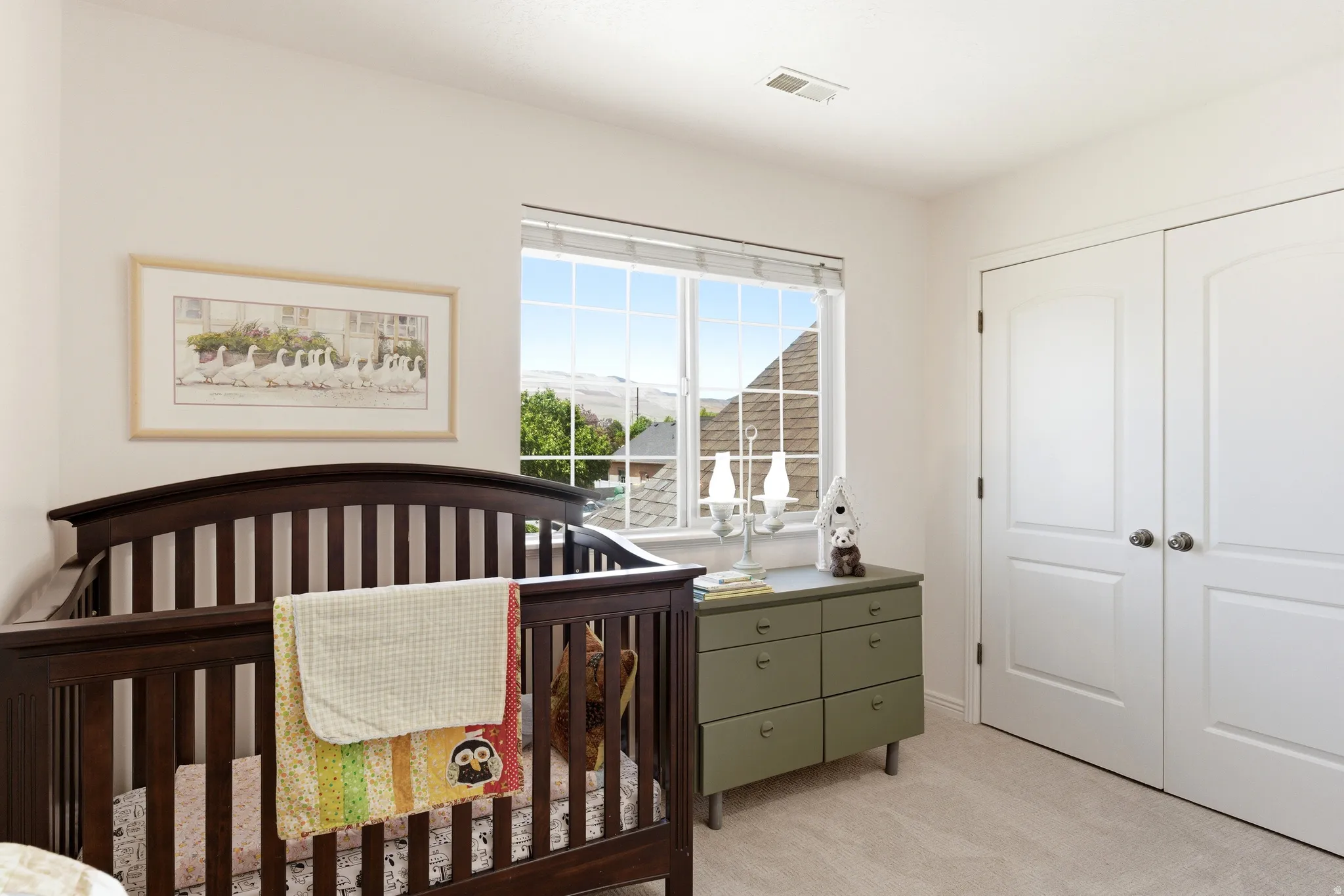 Bright room featuring light neutral wall paint, a large picture window with grid detailing, soft carpet flooring, and a double-door closet with arch paneling