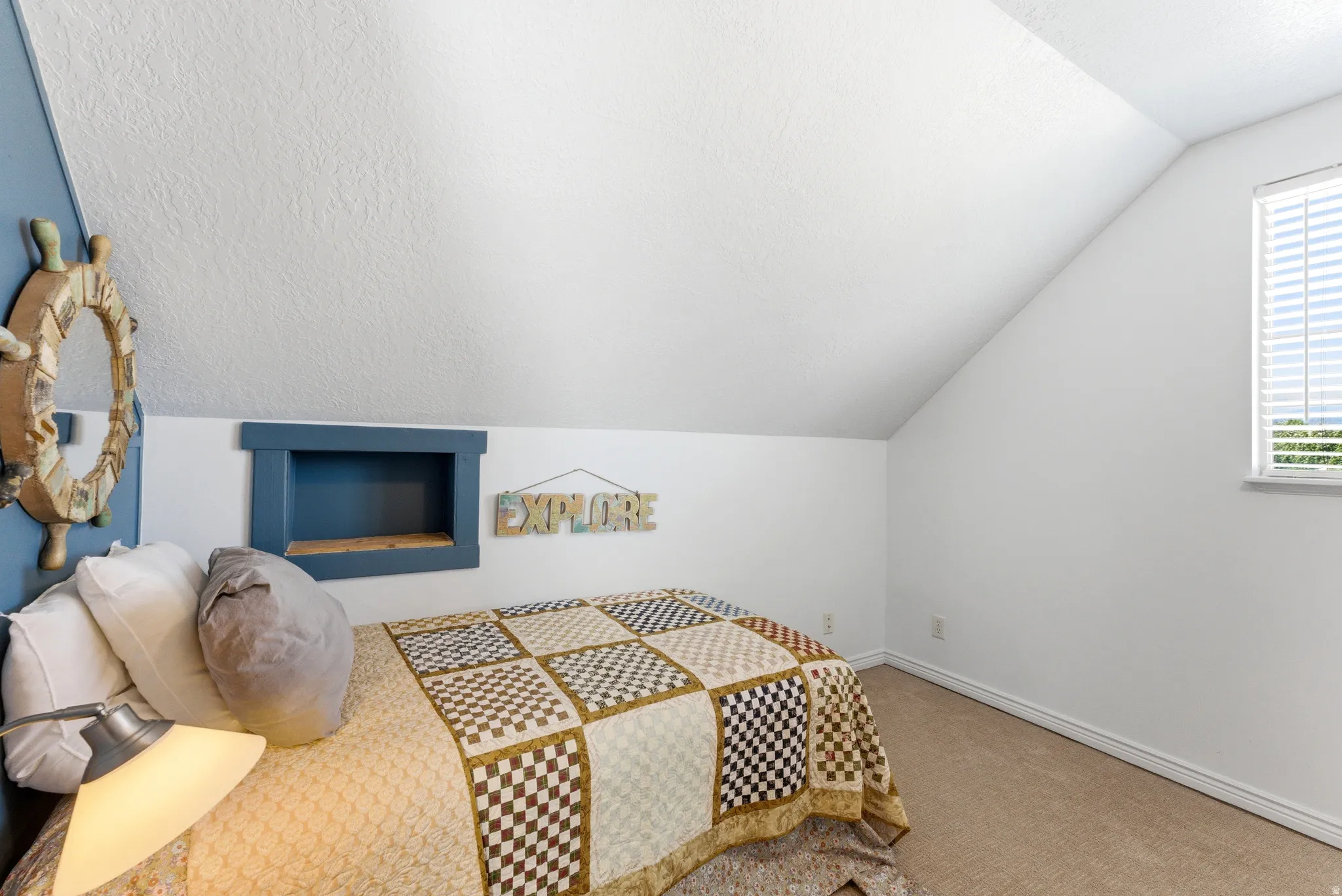 Carpeted room with an angled ceiling and a single window featuring blinds