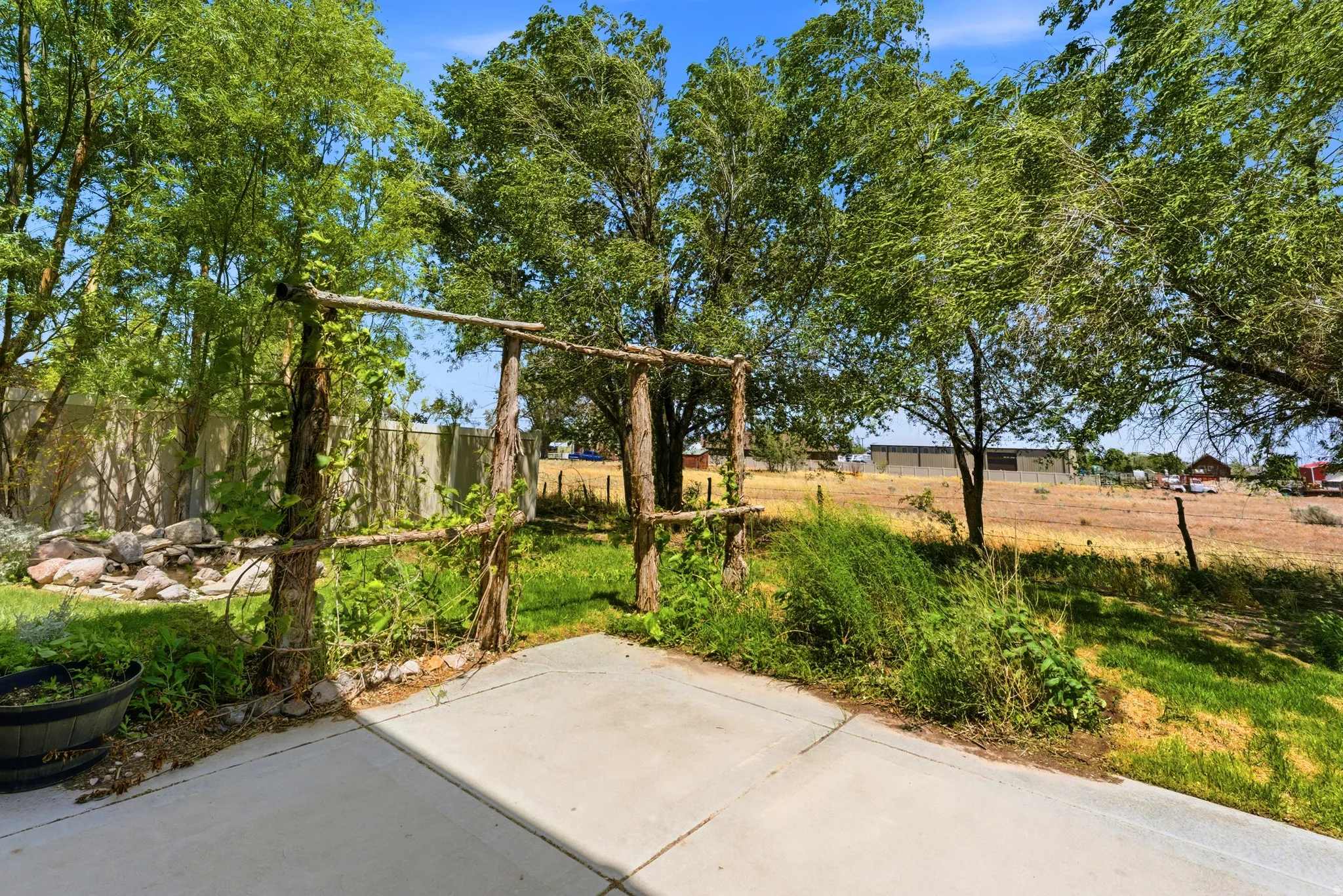 Expansive outdoor patio with a rustic wooden arbor, mature trees providing natural shade, and a rock garden feature