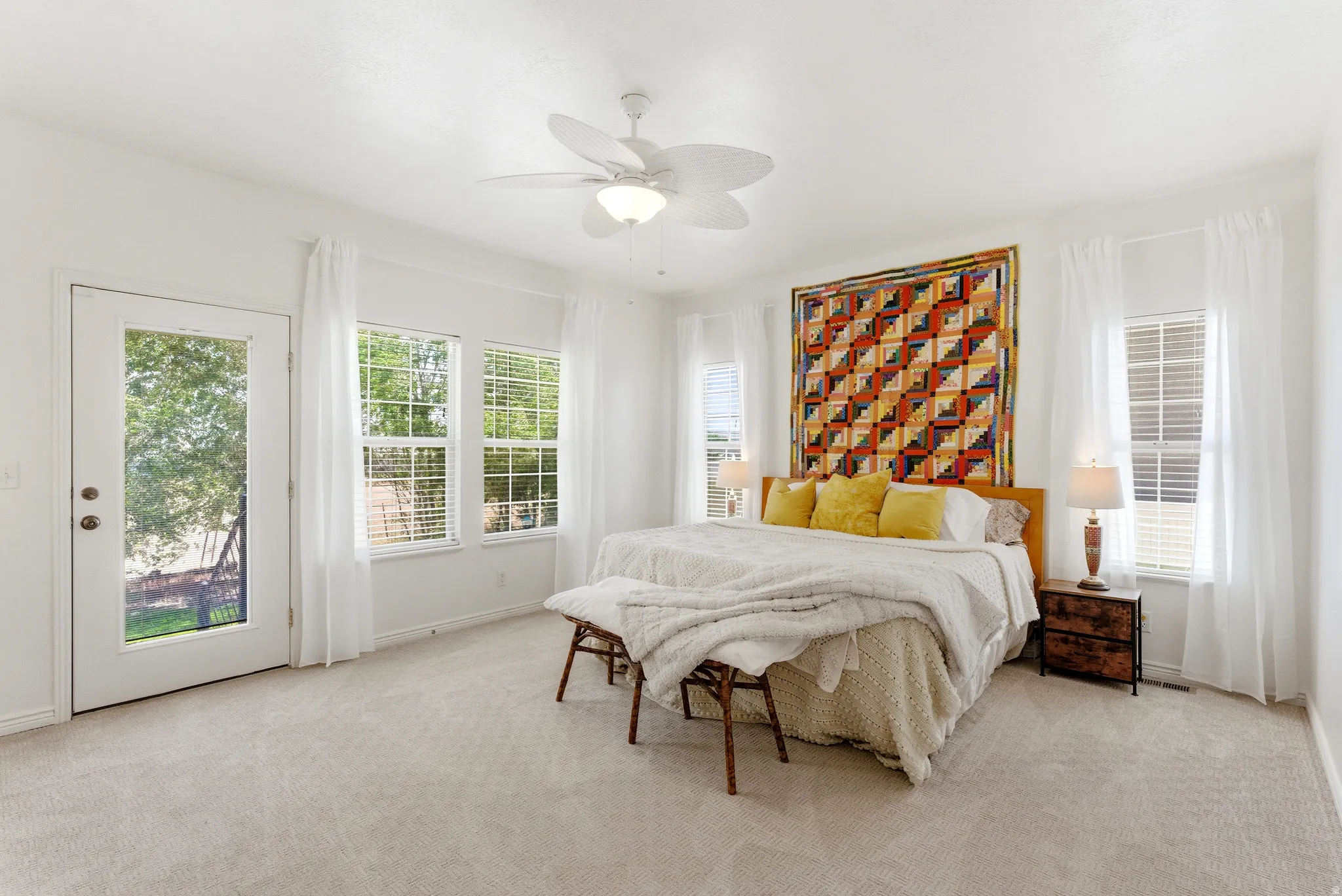 Spacious room featuring light-colored carpeting, multiple windows with blinds, a ceiling fan with integrated lighting, and a glass-paneled exterior door