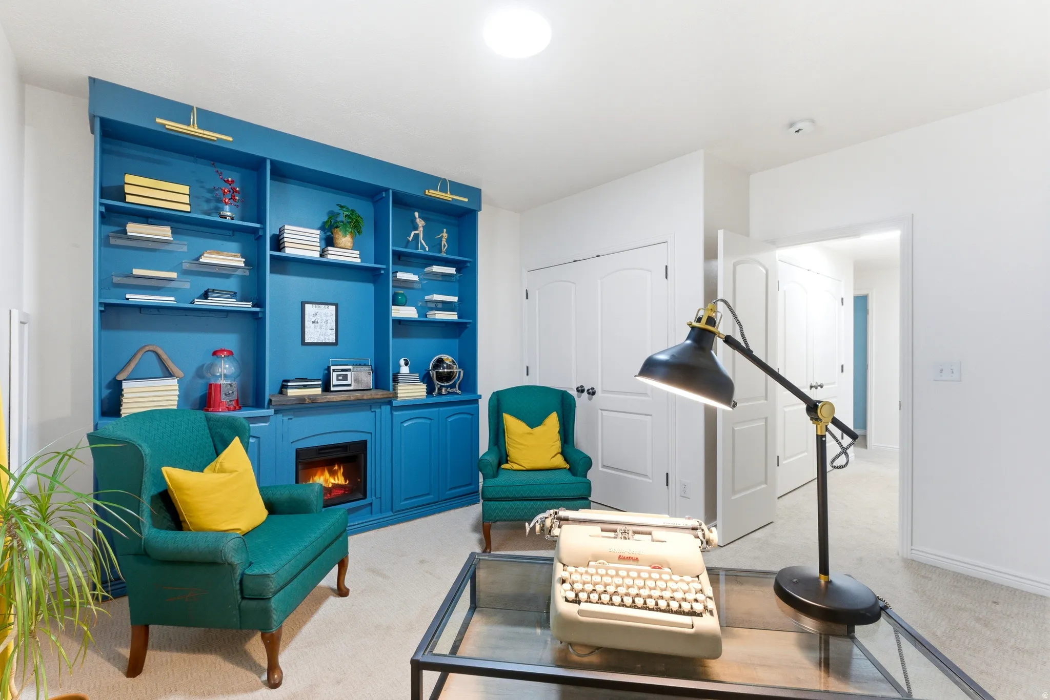 Built-in blue shelving unit with integrated fireplace, white walls, and light-toned carpet flooring.  Used as Office or Bedroom
