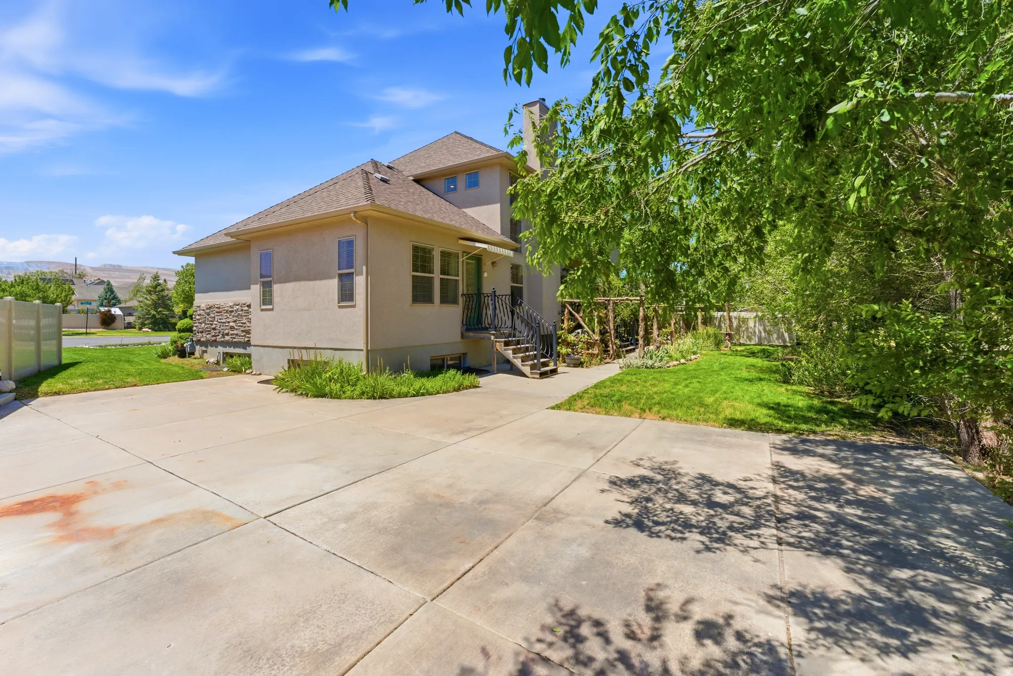 Multi-level exterior featuring stucco and stone veneer, a concrete driveway, established landscaping, and a side yard with mature trees