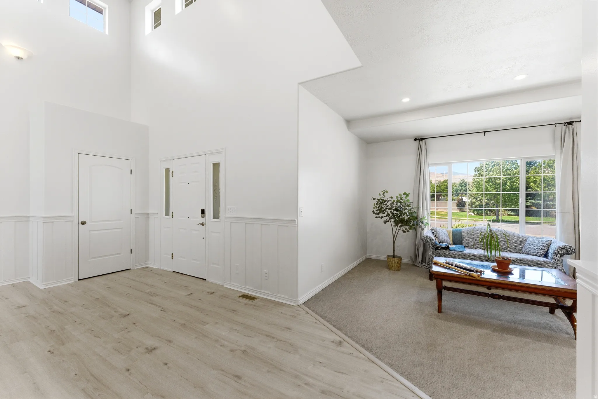 Entryway featuring a double-height ceiling, light wood-finish flooring, wainscoting, and a front door with sidelights