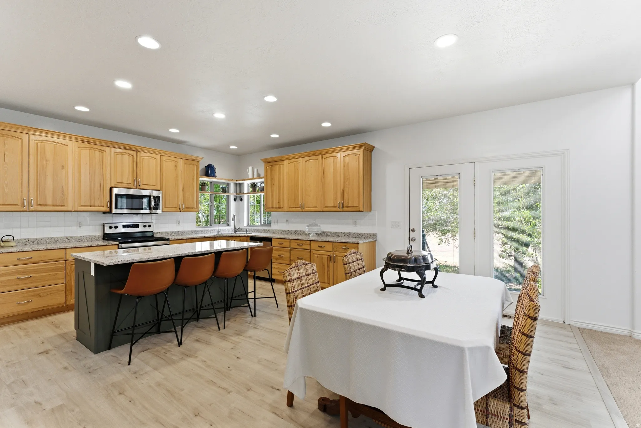 Kitchen featuring light wood cabinetry, stainless steel appliances, a center island with seating, light granite-style countertops, and light wood-finish flooring