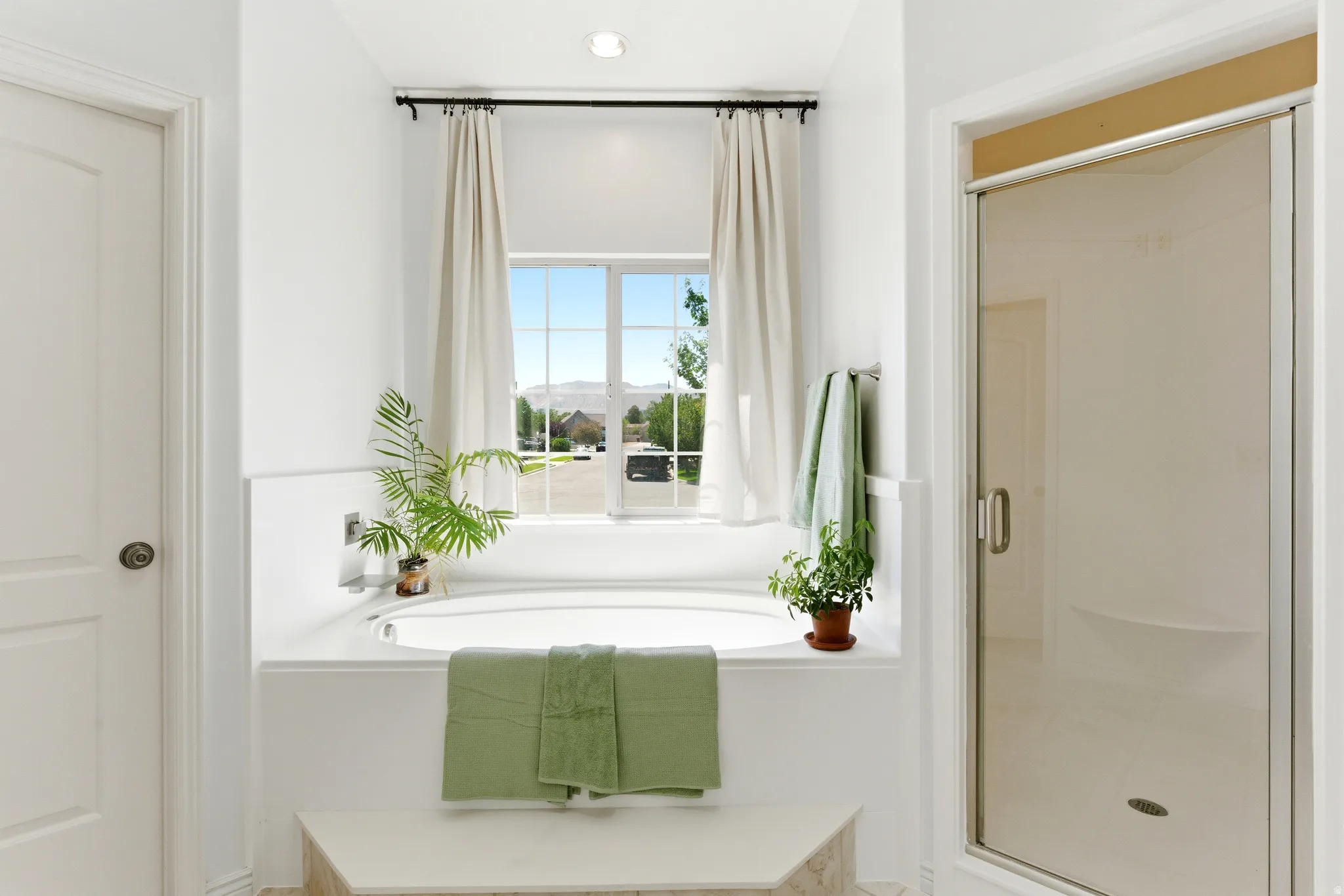 Built-in soaking tub with a tiled surround, framed window, recessed lighting, and a glass-enclosed shower