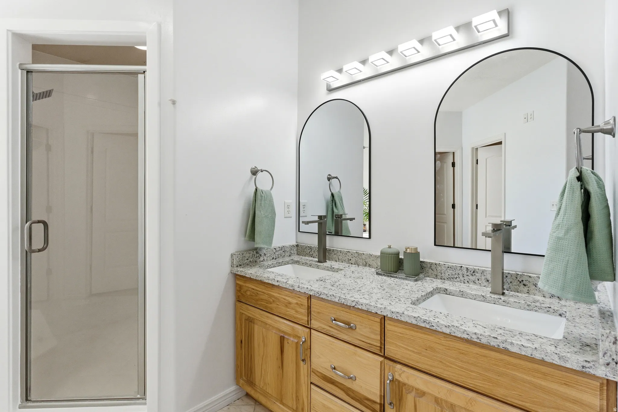 Double vanity with light wood cabinetry and stone countertops