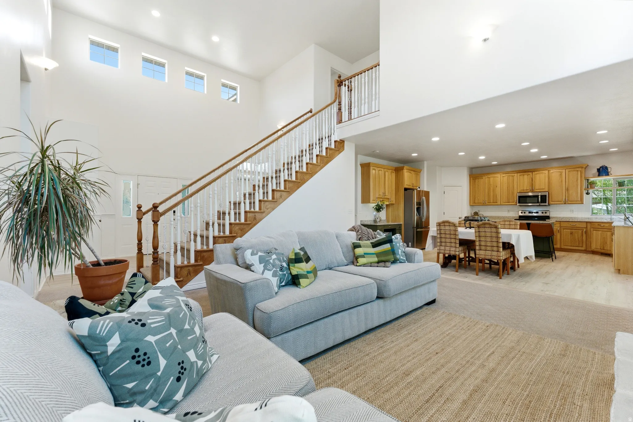 Open-concept living space featuring a high-ceiling entry, a wood staircase with white balusters, and transom windows