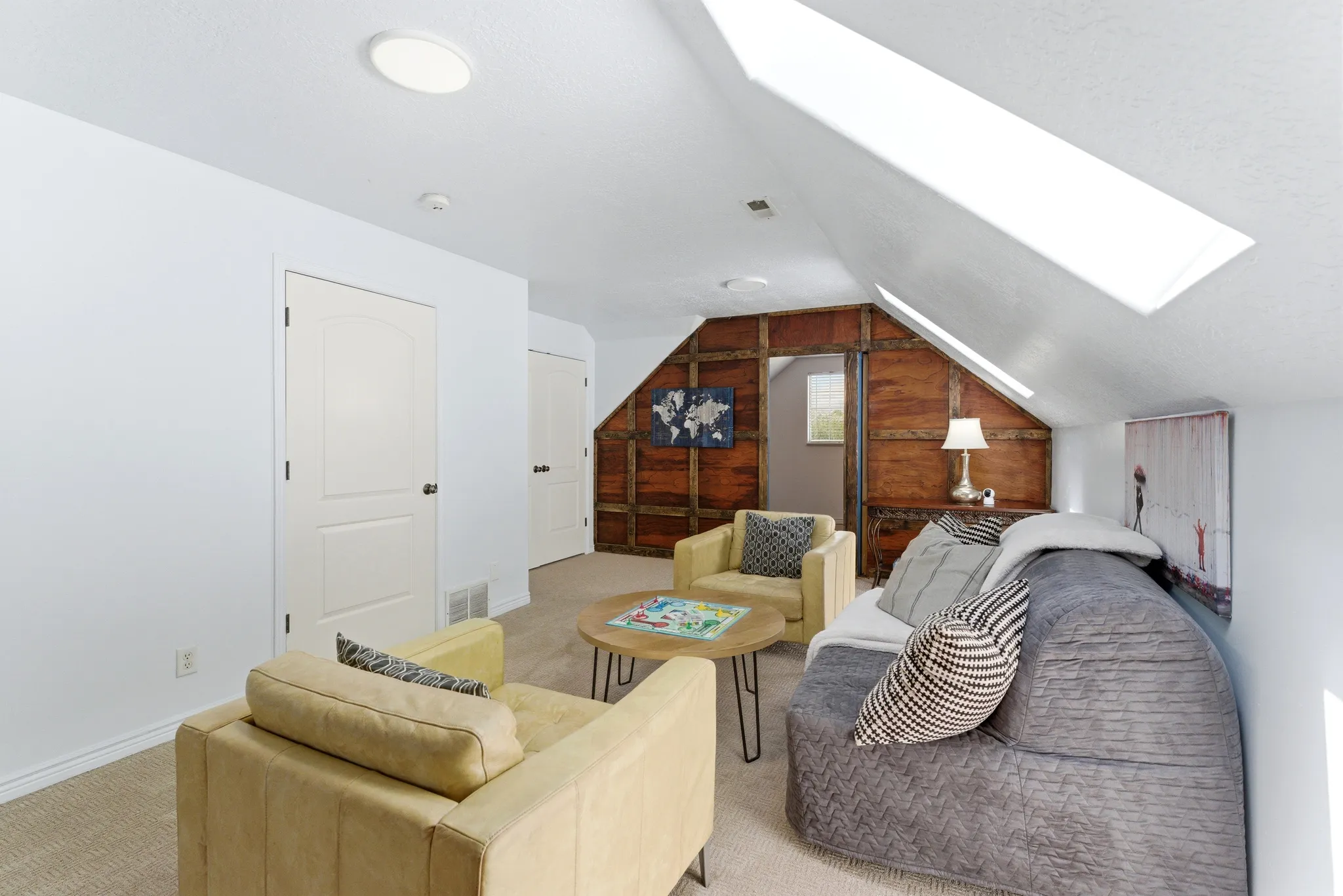 Carpeted loft area featuring a vaulted ceiling with two skylights, an accent wall with wood paneling, and two paneled doors