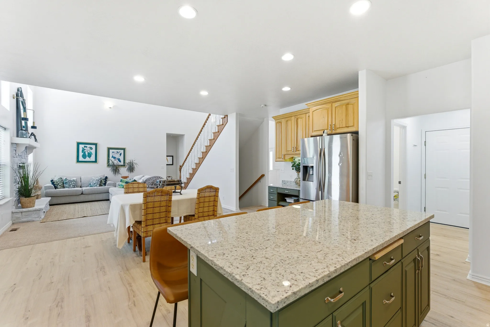 Kitchen island with a granite-style countertop and green cabinetry, wood-finish flooring, recessed lighting, and a stainless steel refrigerator
