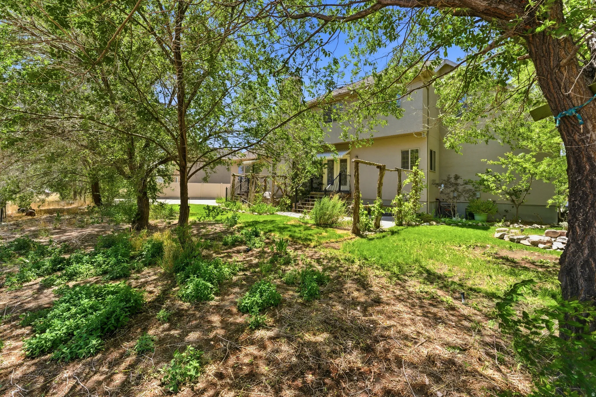 Expansive backyard featuring mature trees, a multi-level deck with wooden pergola, and a stucco exterior