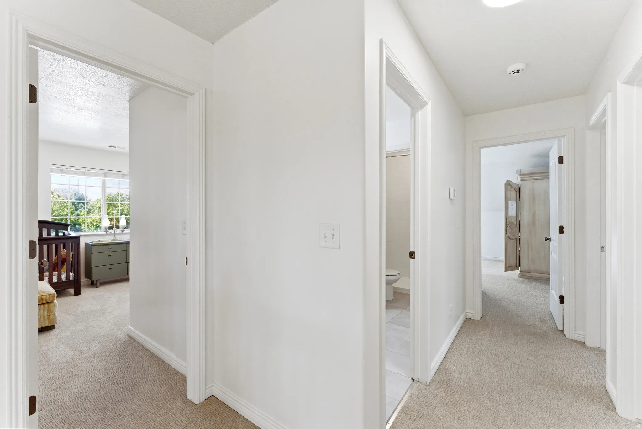Hallway with neutral carpeting and white painted walls, featuring multiple doorways leading to other rooms
