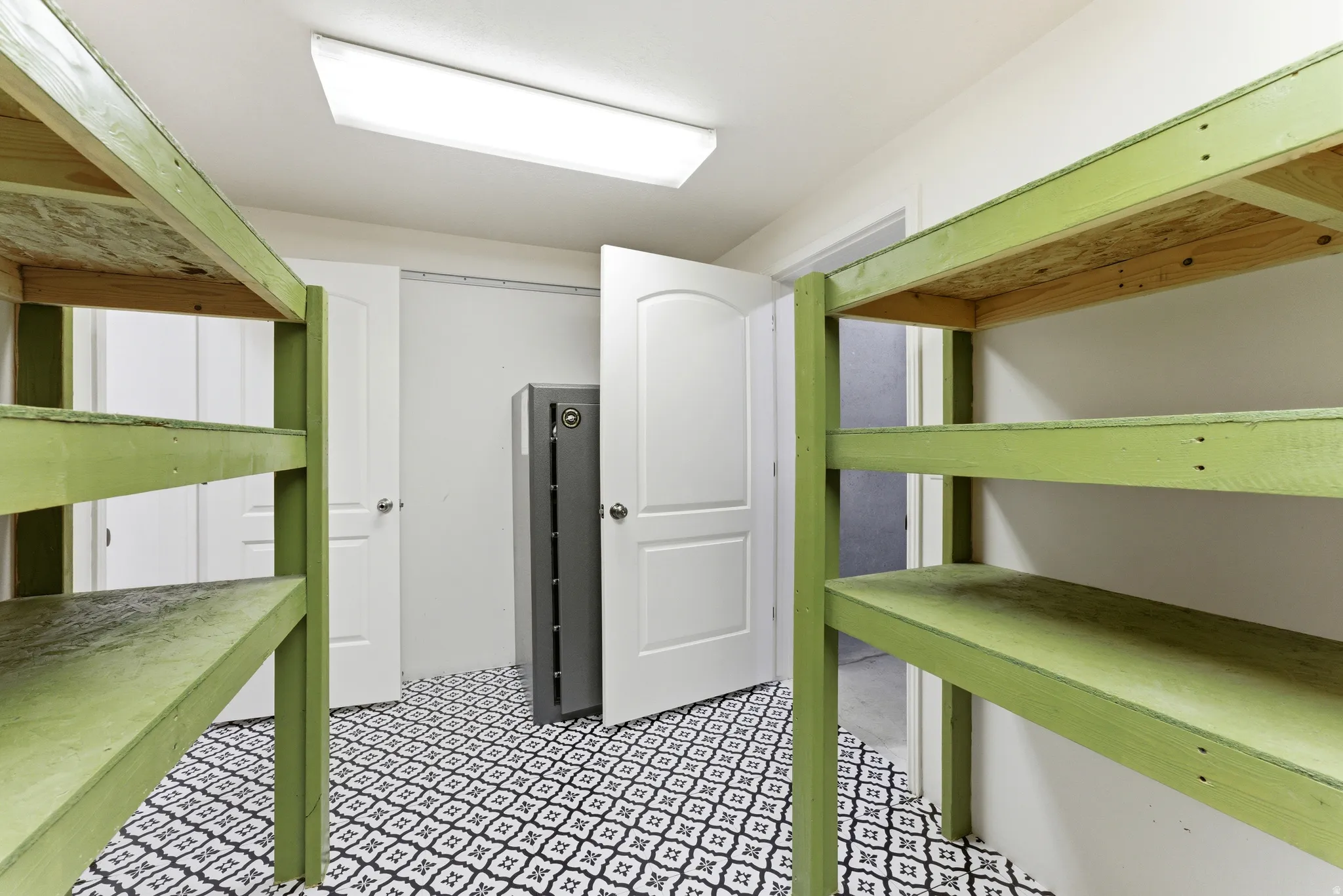Dedicated storage room featuring patterned tile flooring, two white panel doors, and two sets of open-face shelving
