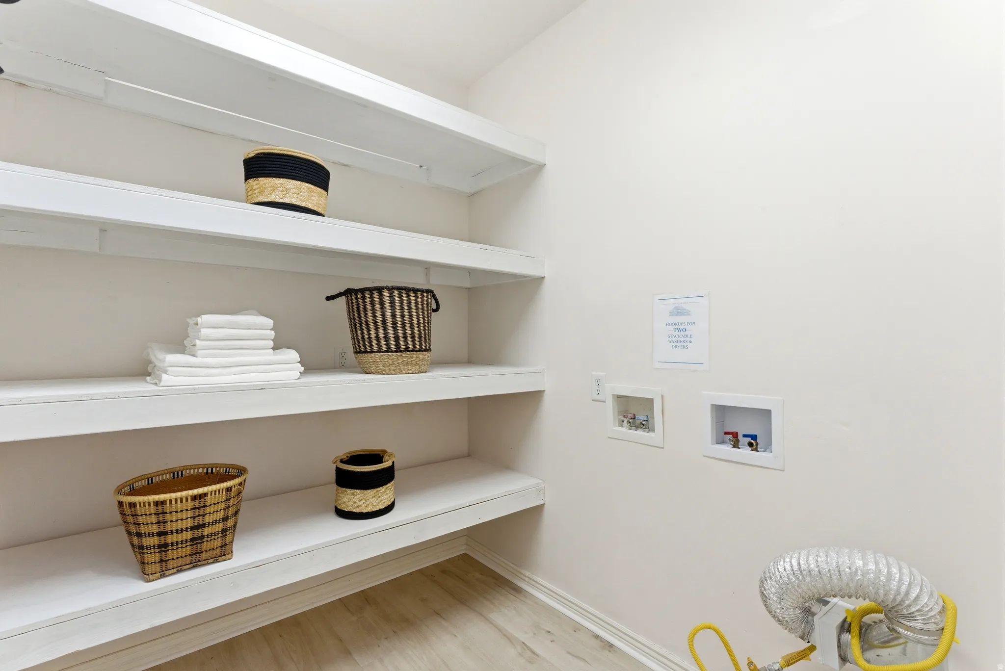 Dedicated utility space featuring extensive built-in shelving, light wood-finish flooring, and wall-mounted water hookups