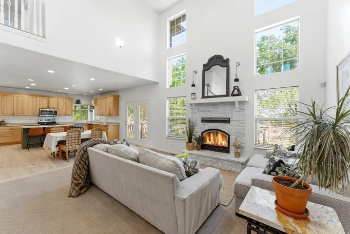 Two-story living area featuring a stone-clad fireplace with mantel, high ceilings, multiple large windows, and recessed lighting