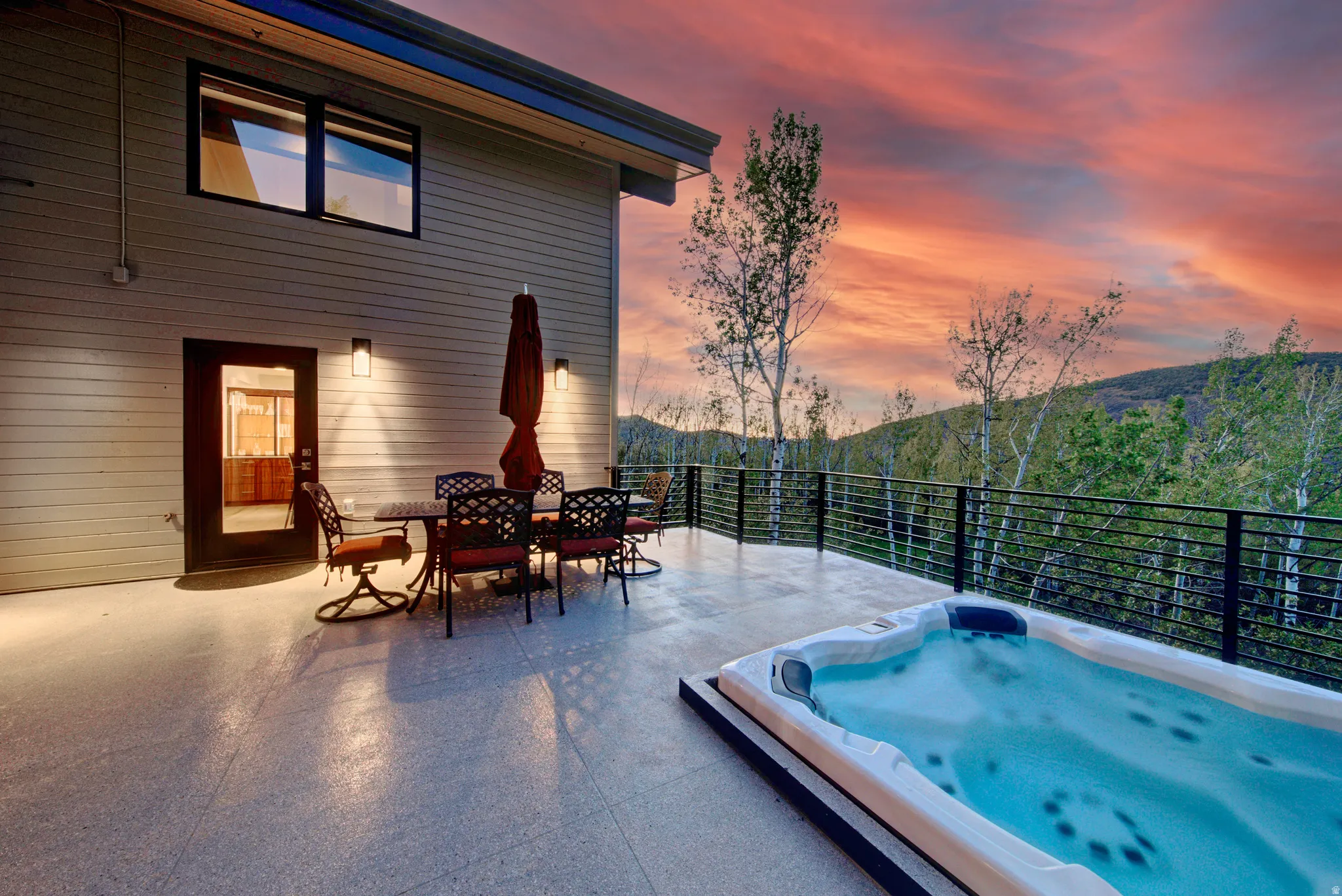 Expansive outdoor deck featuring a built-in spa, horizontal metal railings, and integrated wall sconces