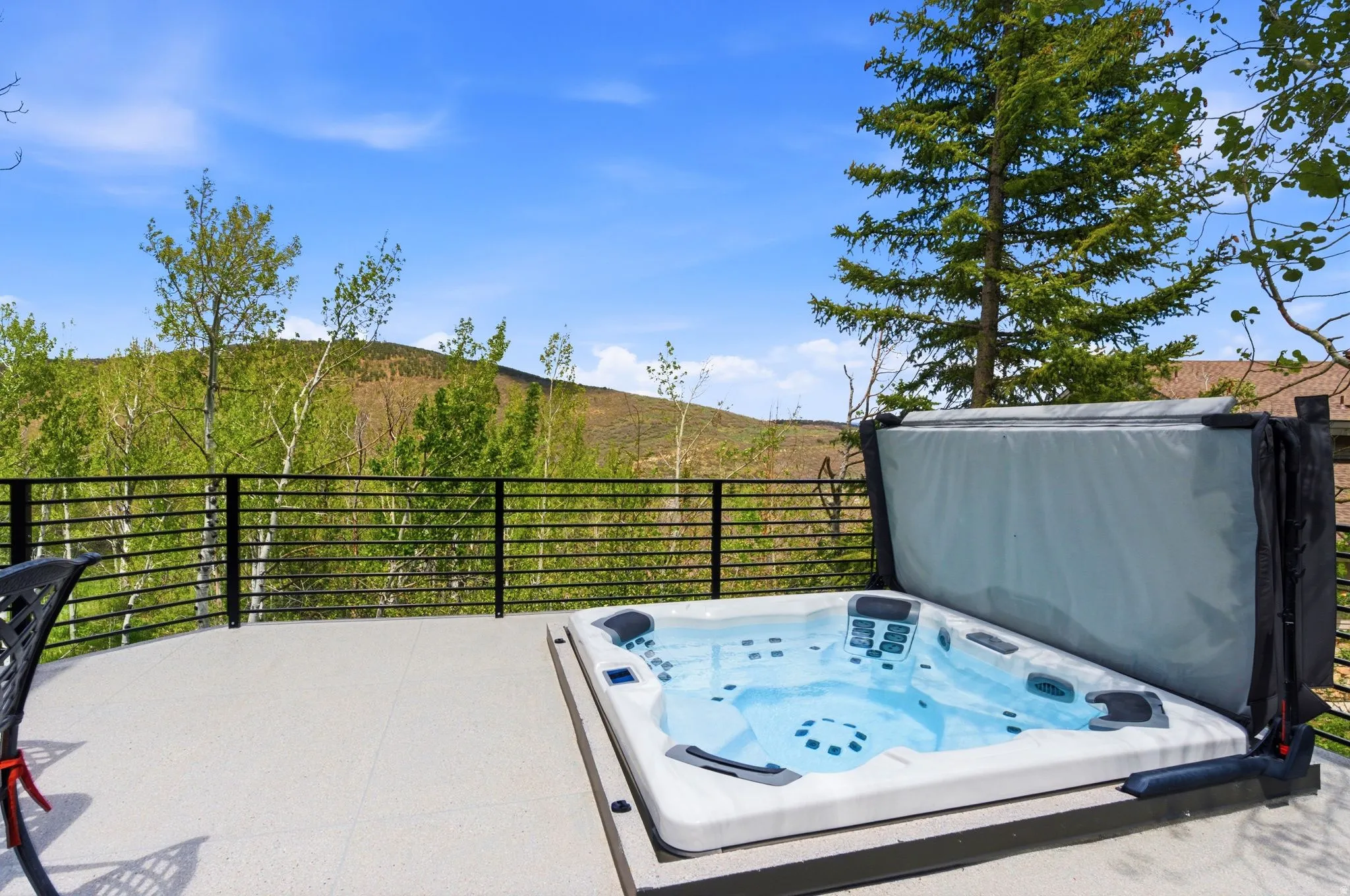 Outdoor hot tub with a solid cover, set on a spacious patio with a horizontal slat railing