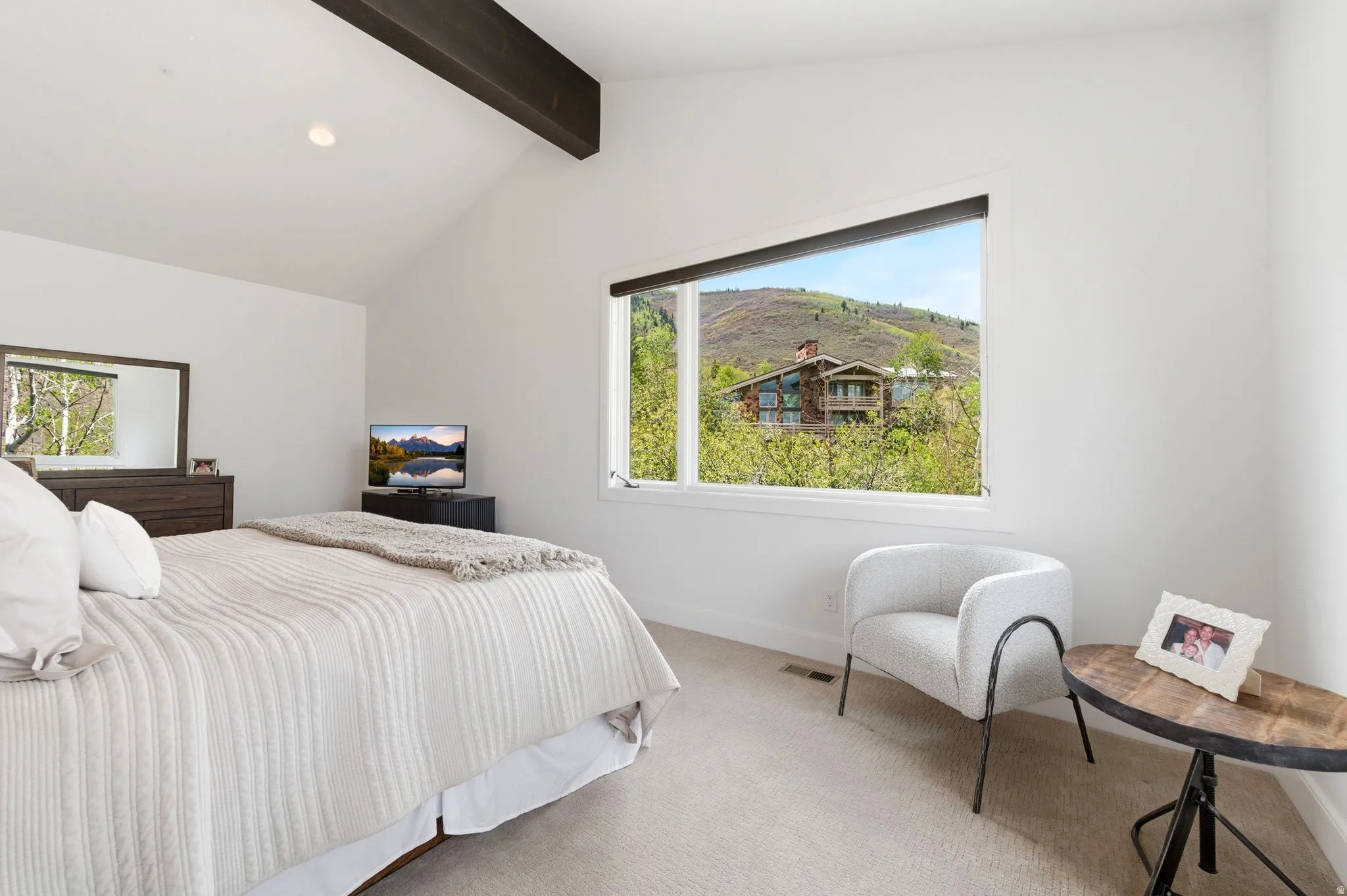 Vaulted ceiling with exposed wood beam, large picture window, recessed lighting, and carpeted flooring
