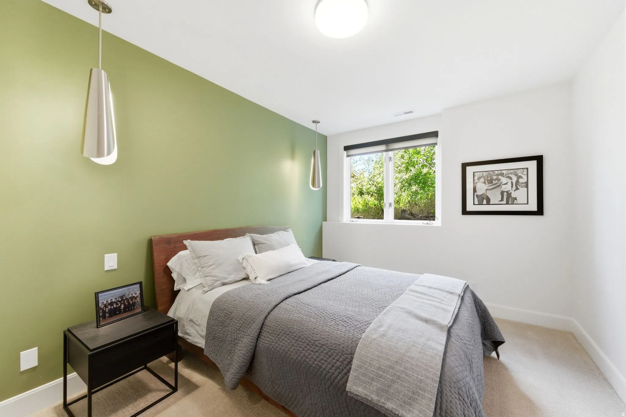 Bedroom featuring a contrasting accent wall, two pendant light fixtures, and a large window with roller shades