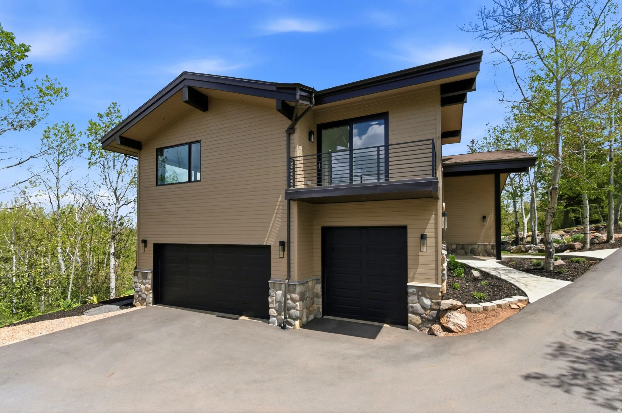 Modern architectural design featuring stacked stone accents, a private balcony with horizontal railings, and dual garage doors