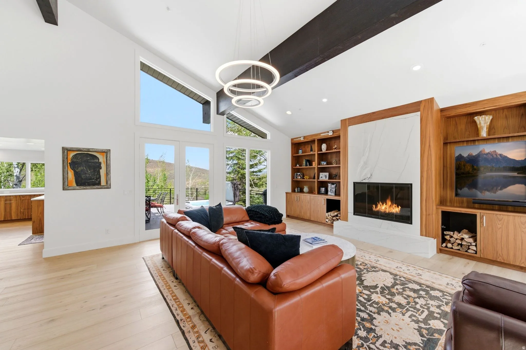 Vaulted ceiling living area featuring a stone-surround fireplace, custom wood built-in shelving, wood-finish flooring, ample natural light, and direct access to an outdoor area via double glass doors