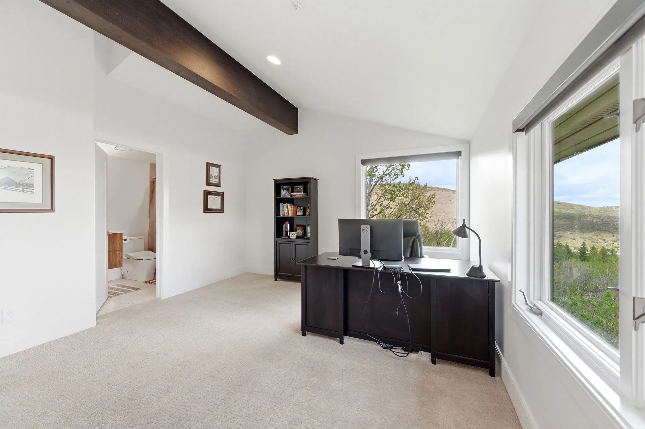 Vaulted ceiling room with an exposed dark wood beam, light carpet flooring, and white walls