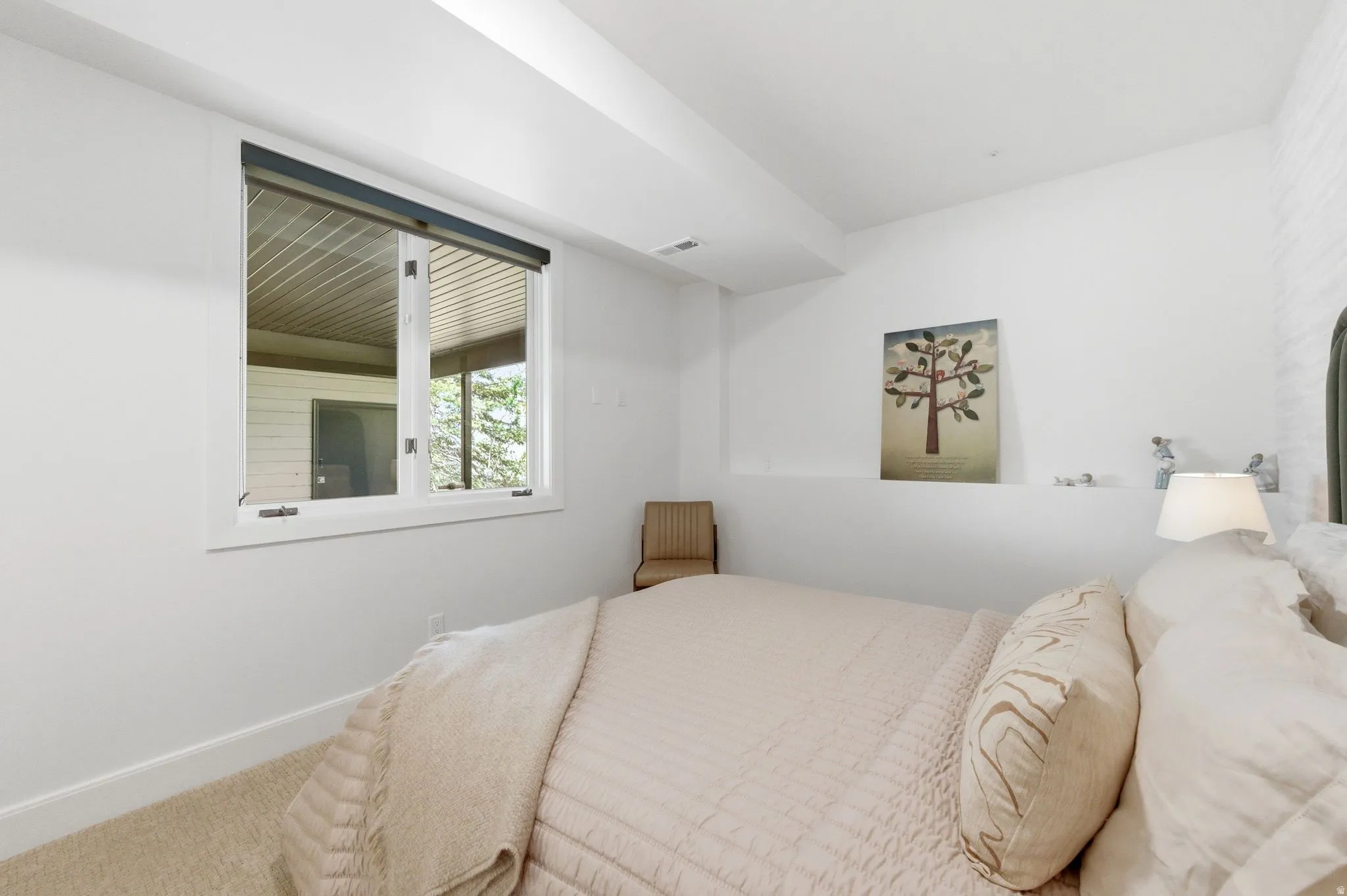 Bedroom with light-colored carpeting, white baseboards, and a window with a dark roller shade