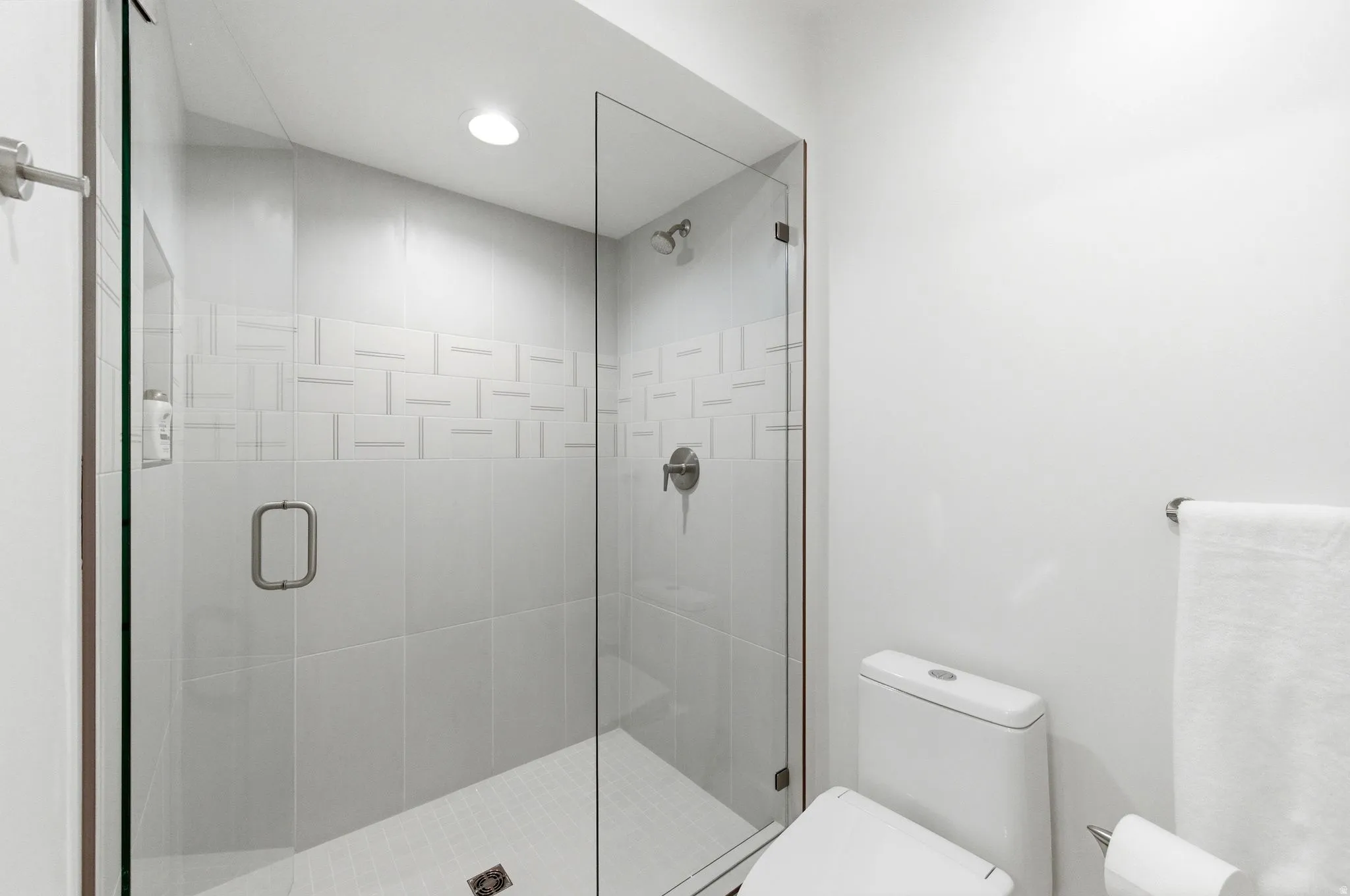 Walk-in shower featuring a frameless glass enclosure, a tiled accent band with a geometric pattern, recessed lighting, and a brushed nickel shower head