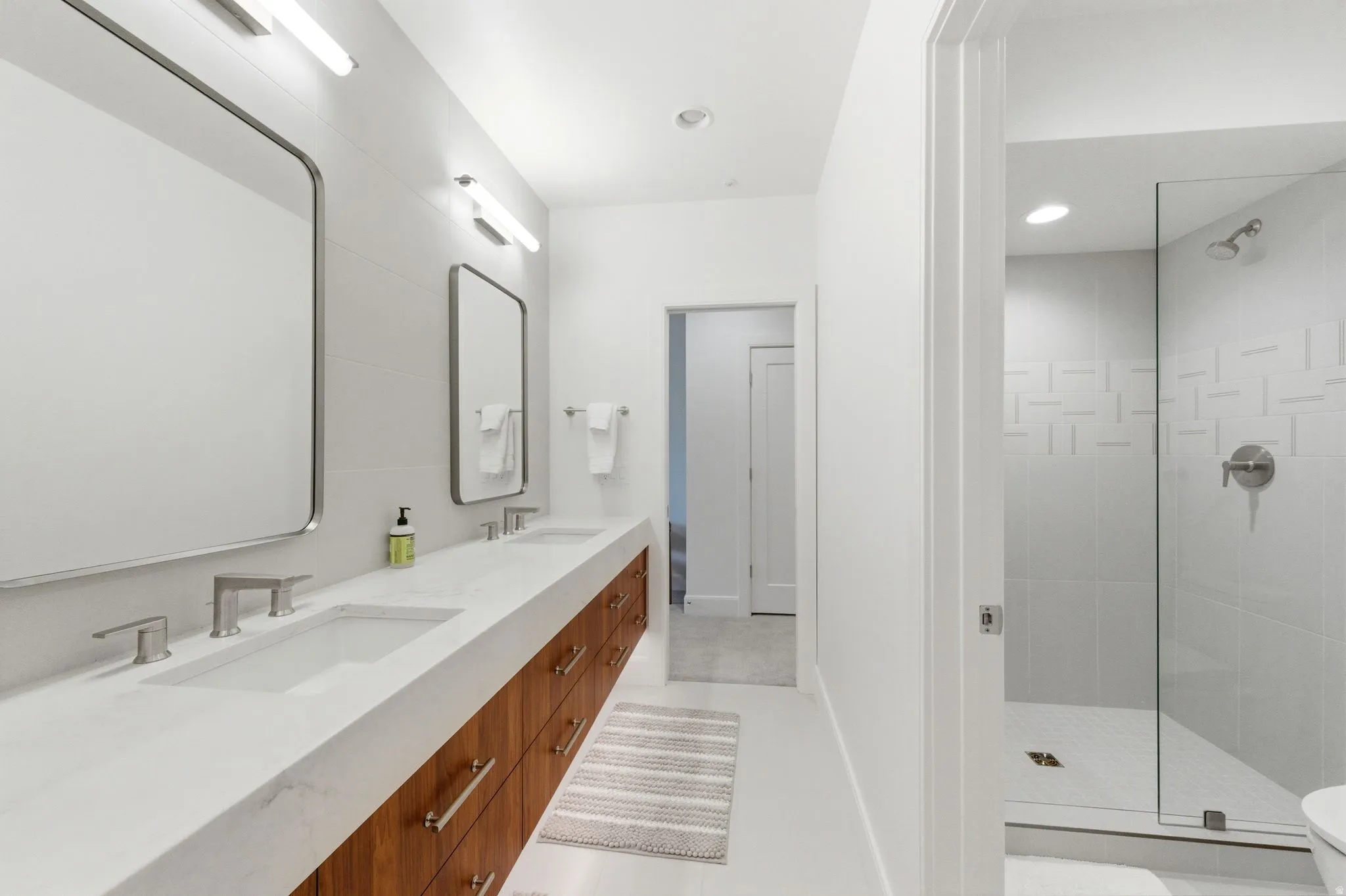 Bathroom featuring a dual vanity with a light-toned countertop and wood-finish cabinetry, rectangular undermount sinks, and wall-mounted mirrors