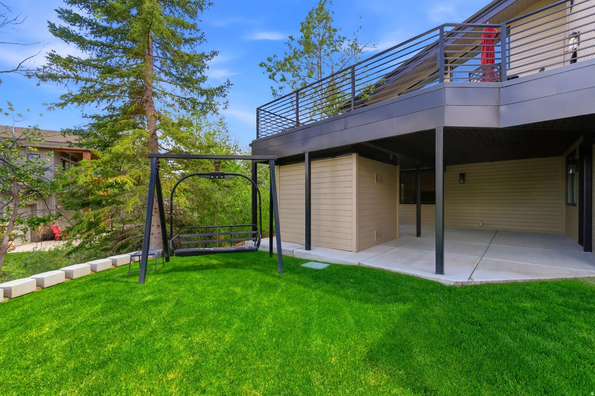 Tiered outdoor living spaces featuring a lower-level concrete patio, an upper-level deck with metal railings, and a retaining wall bordering the lawn