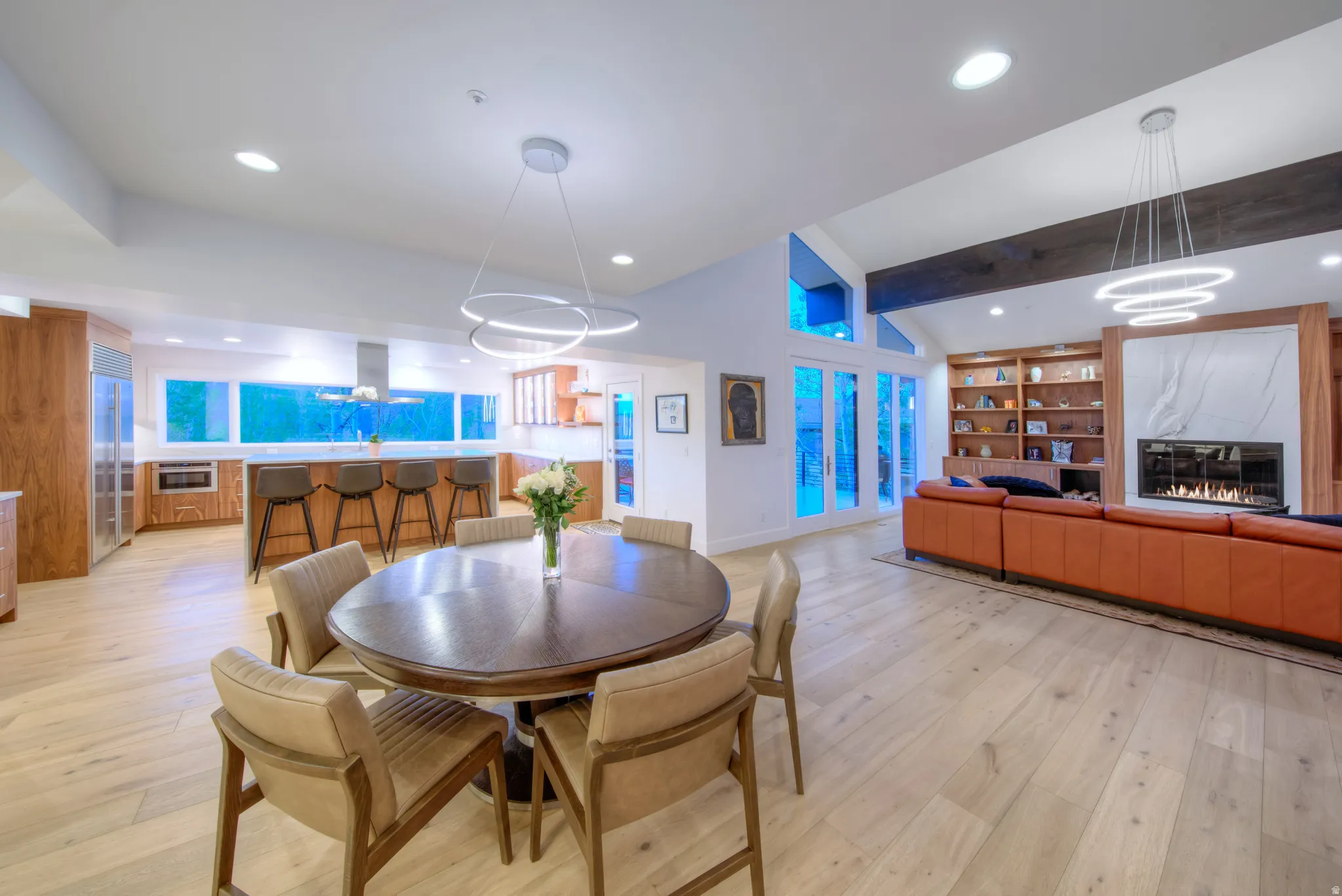 Expansive open-concept living space featuring wood-finish flooring, a contemporary fireplace with a large stone surround, and an integrated kitchen with a breakfast bar
