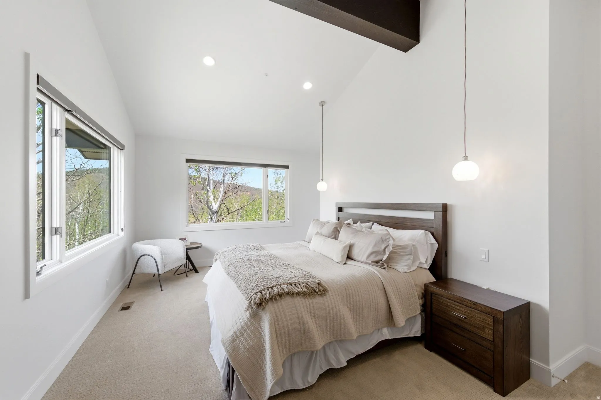 Bright bedroom featuring a vaulted ceiling with exposed beam, recessed lighting, and wall-mounted pendant lights
