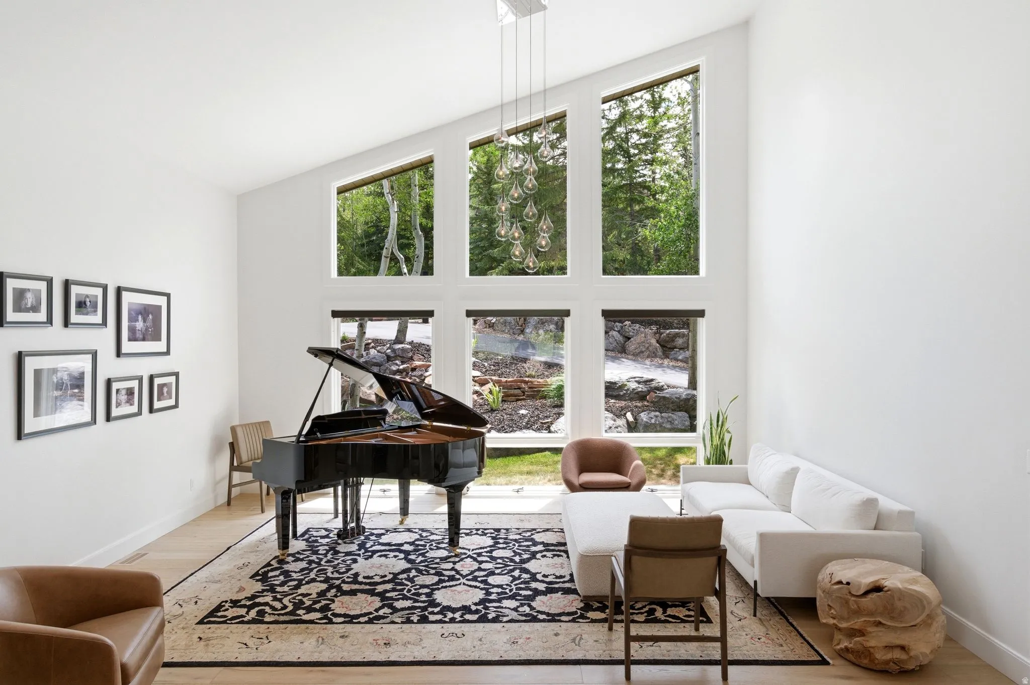 Vaulted ceiling living area featuring a multi-pane window wall, light wood-finish flooring, and a contemporary chandelier