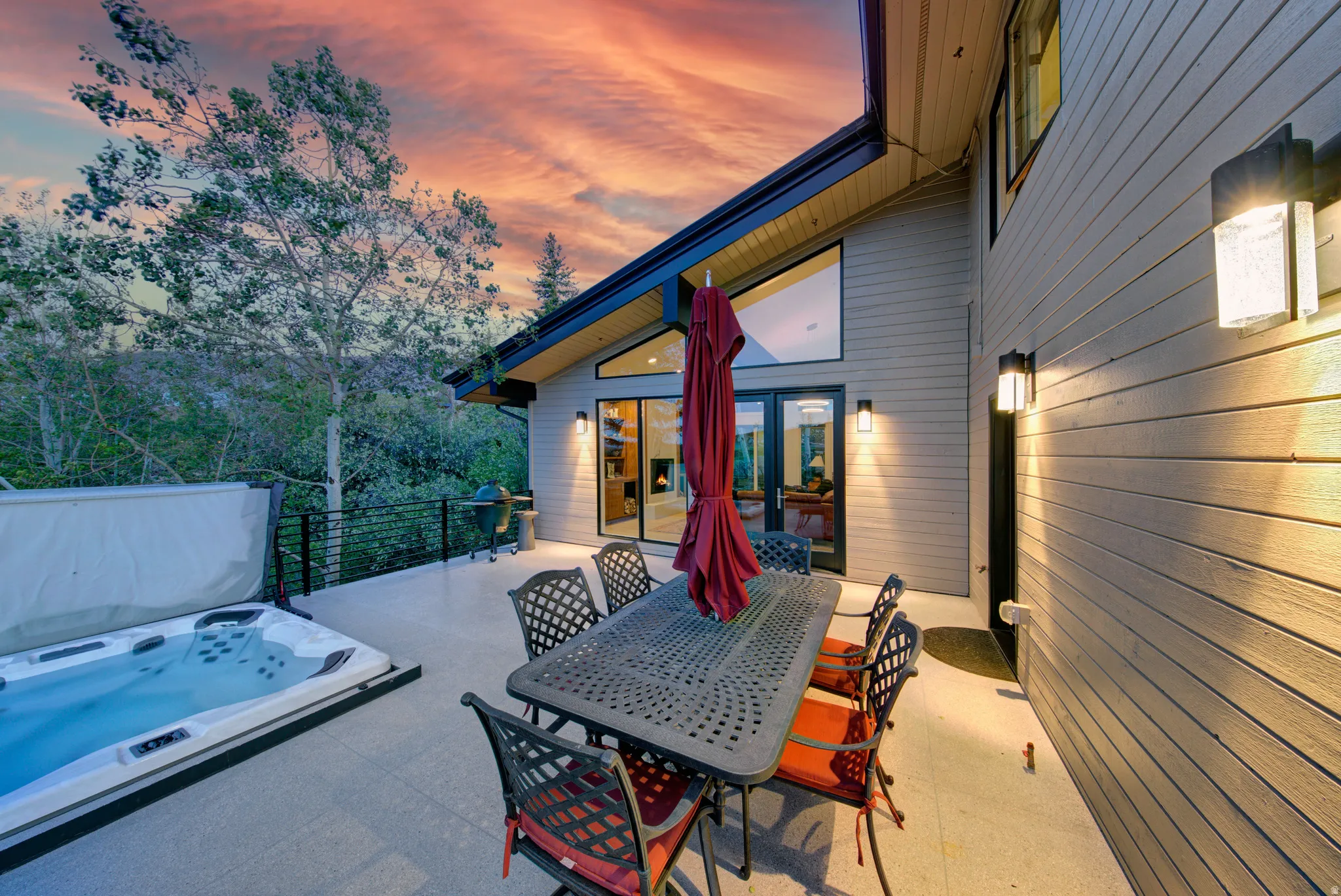 Spacious outdoor patio featuring an integrated hot tub, extensive wall siding, exterior lighting fixtures, and large picture windows