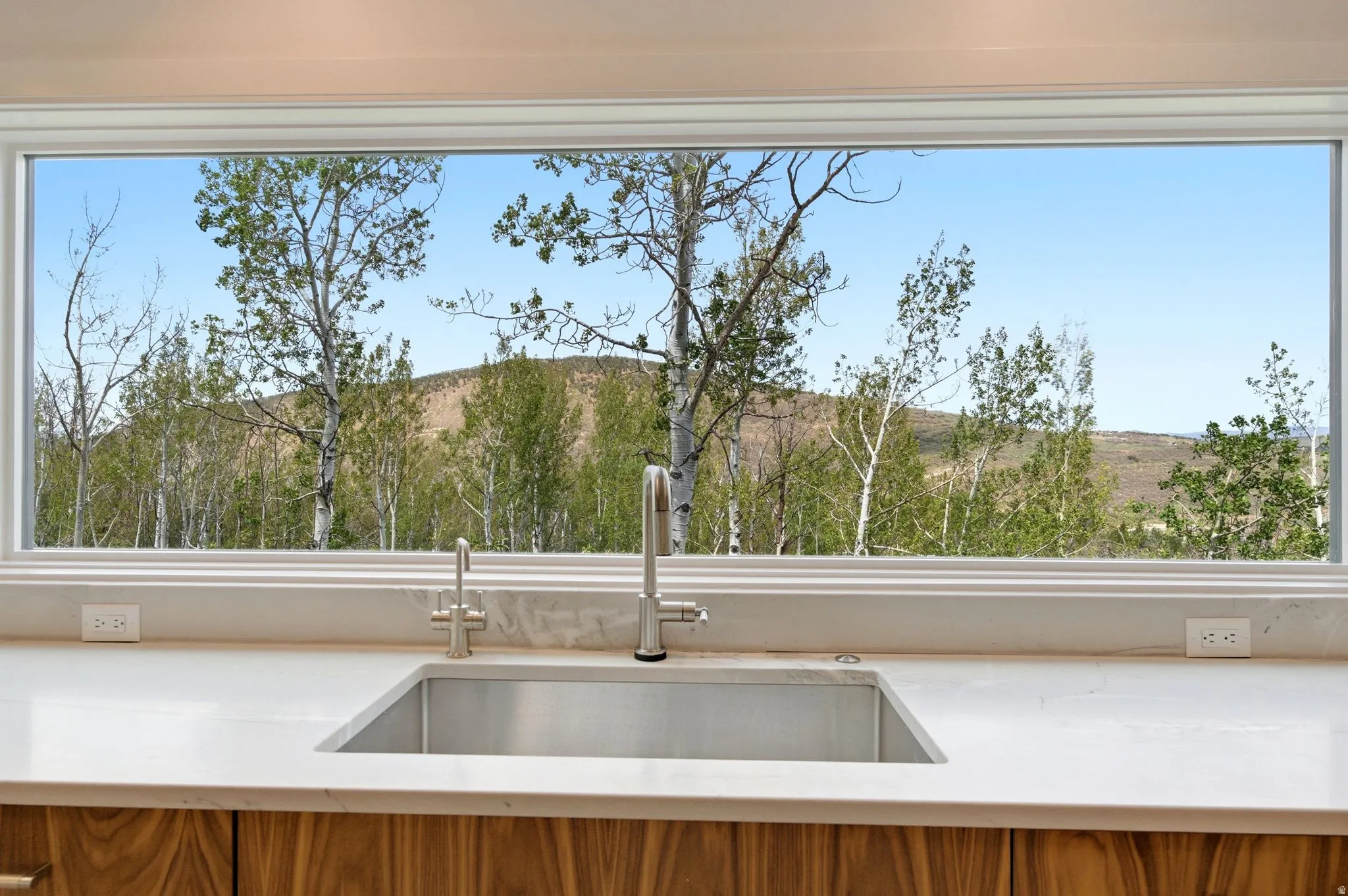 Kitchen sink with a large horizontal window showcasing a natural landscape with trees and distant hills