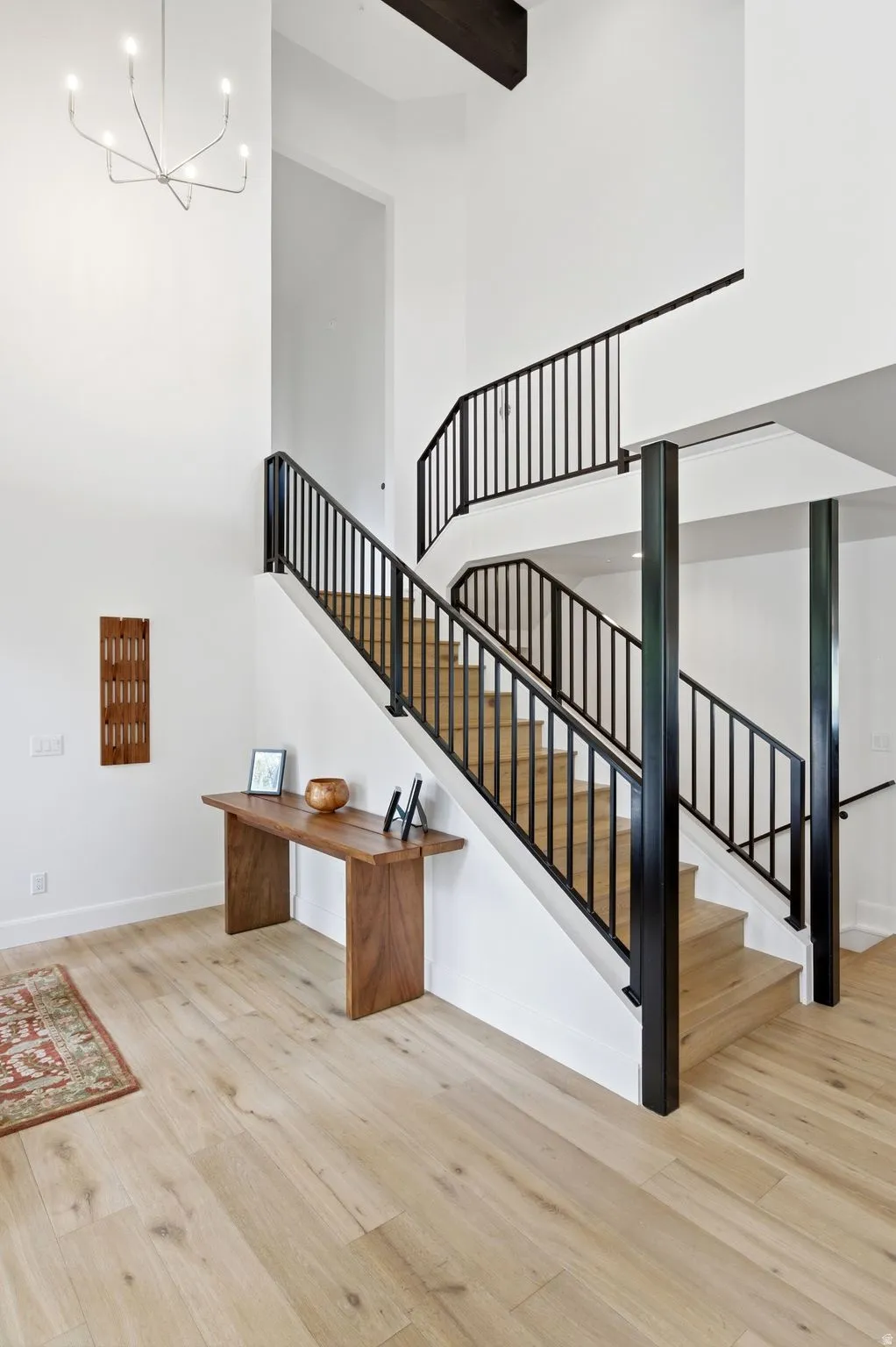 Two-story foyer featuring a contemporary chandelier, open-tread staircase with black metal railings, and wood-finish flooring