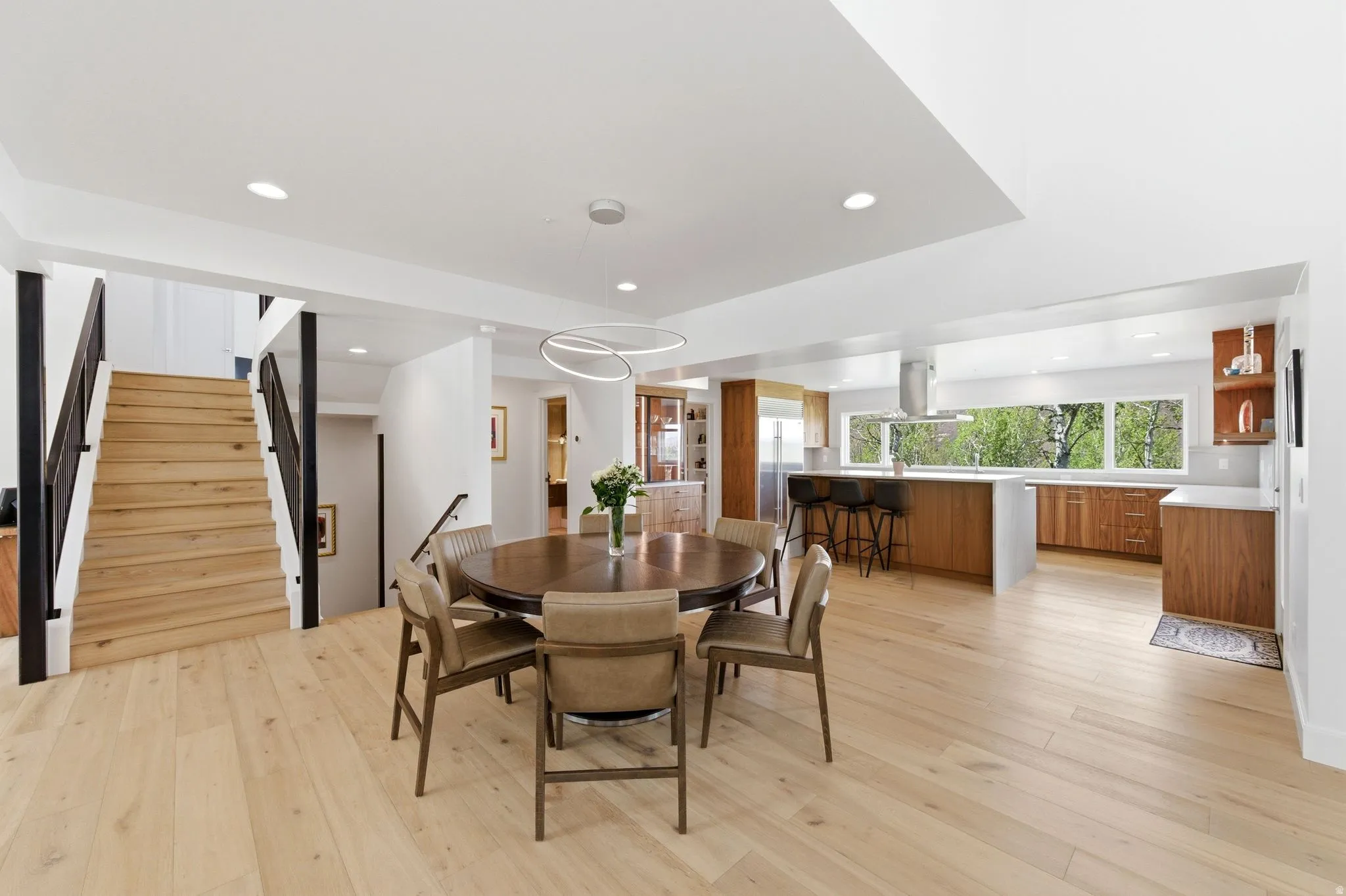 Bright, open-concept living space featuring light wood-finish flooring, a modern kitchen with a large island, stainless steel appliances, and abundant natural light from wide windows