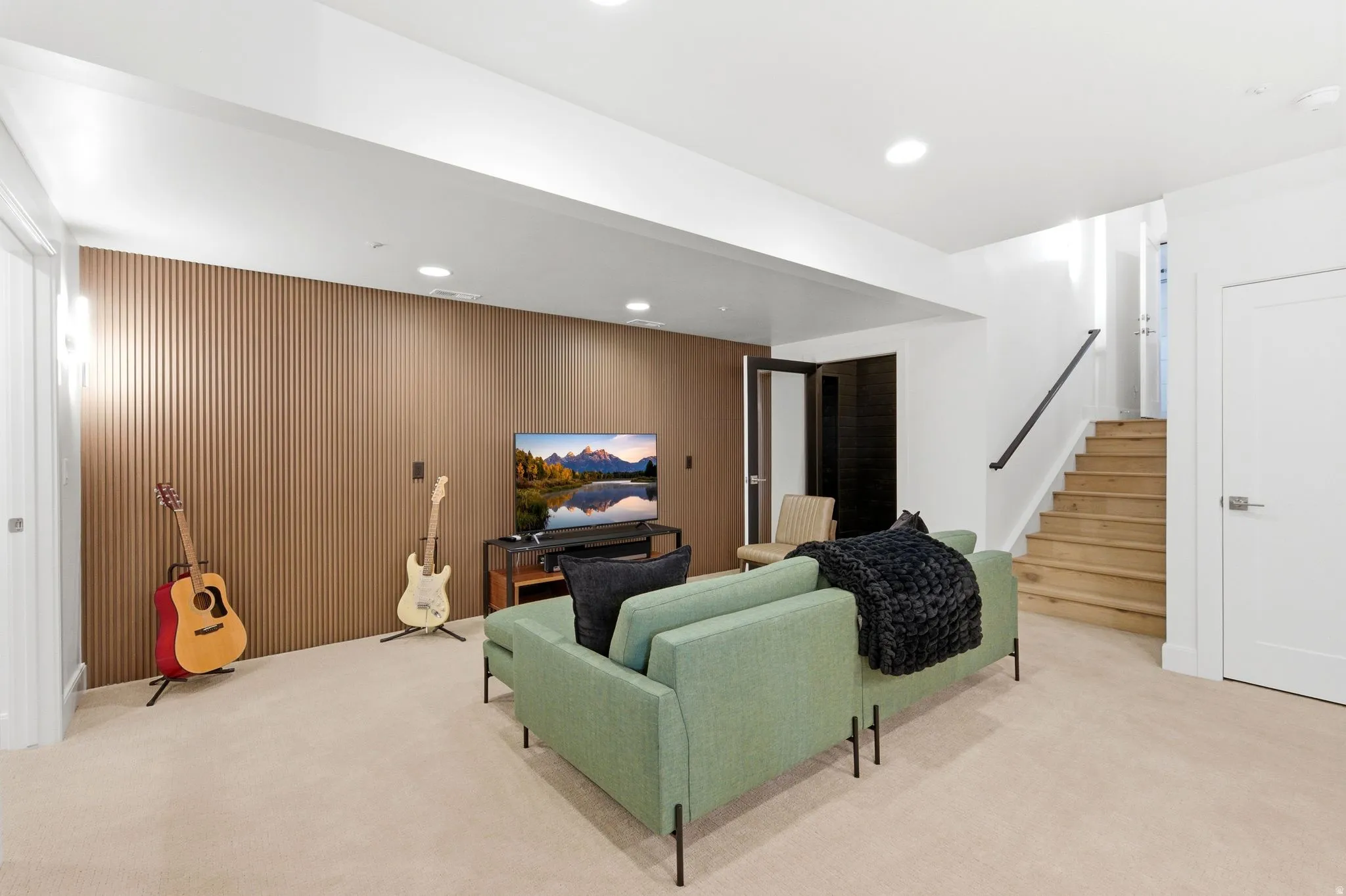 Spacious room featuring a slatted wood-finish accent wall, neutral carpeting, recessed lighting, and a wood staircase with a black metal handrail