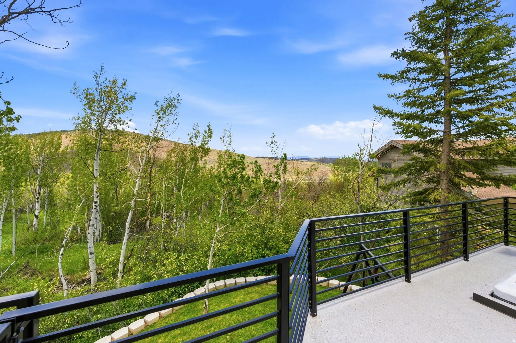 Outdoor terrace with dark metal horizontal railings, overlooking a verdant hillside with varied tree species
