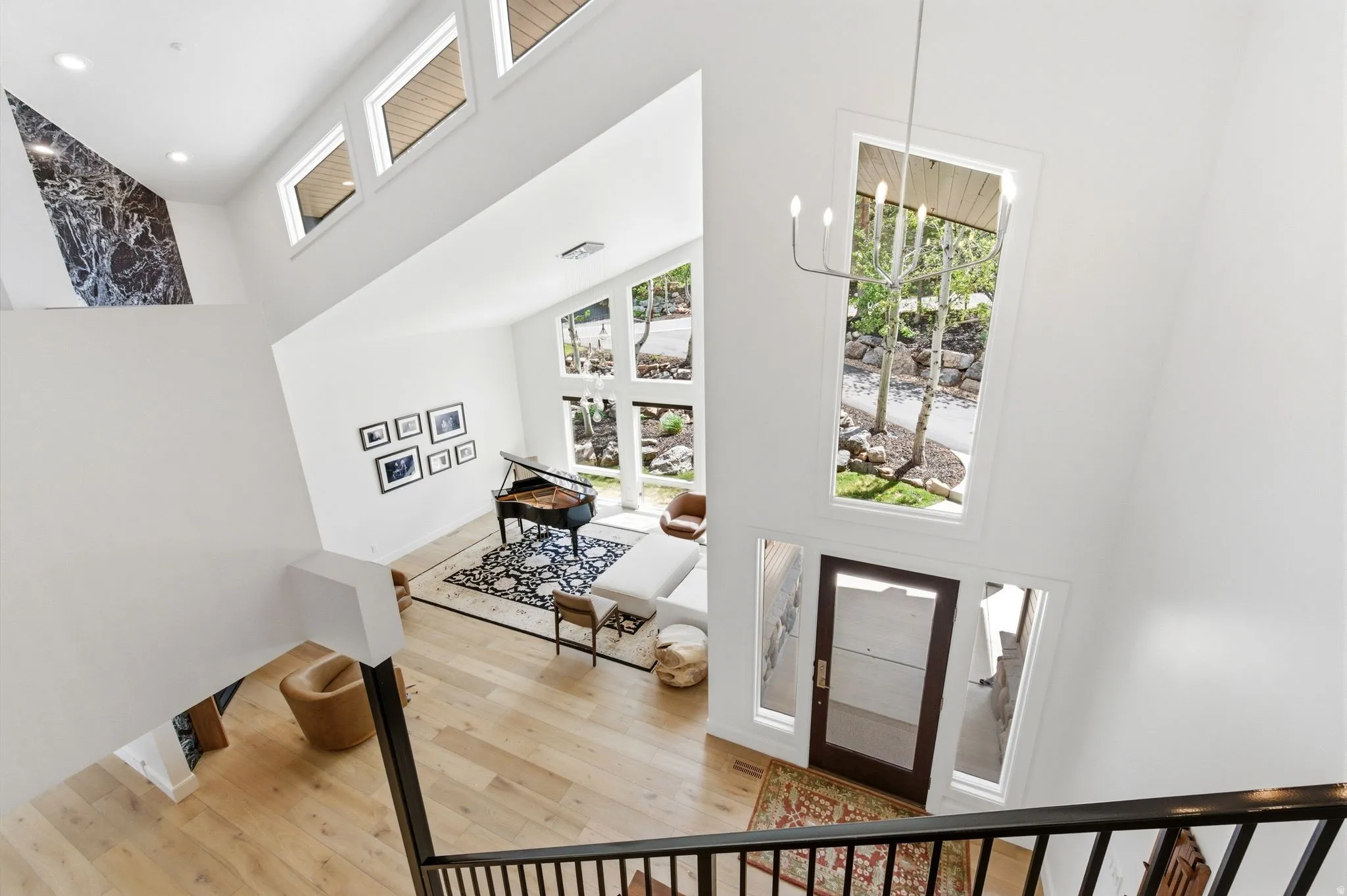 Double-height entry foyer featuring a modern chandelier, light wood-finish flooring, and a dark wood-finish entry door with clear glass panels