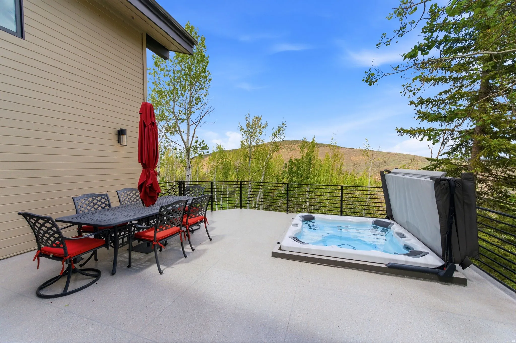 Spacious outdoor deck featuring a hot tub, a built-in outdoor lighting fixture, and a black metal railing overlooking a natural landscape