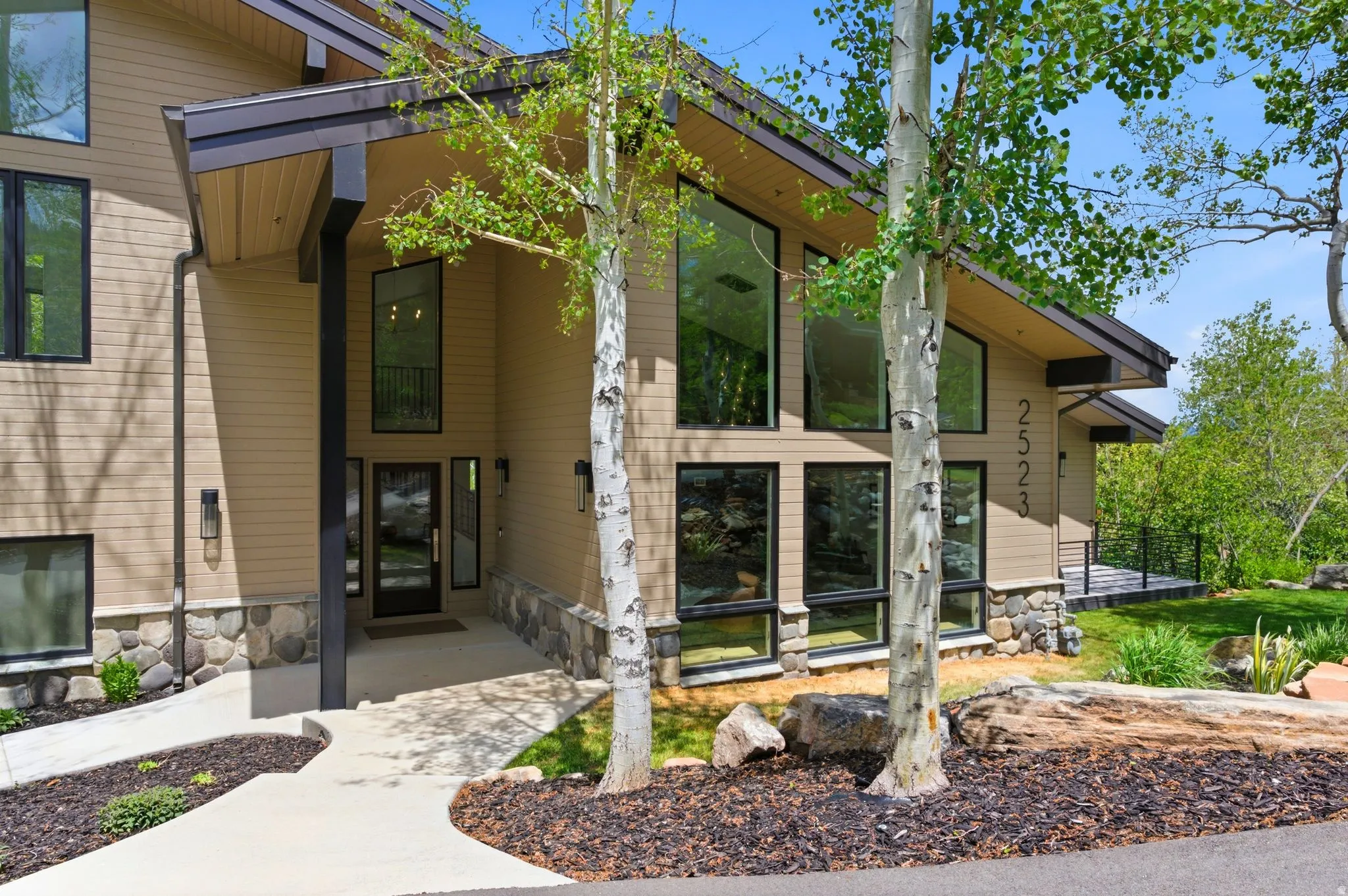 Contemporary exterior featuring tan siding and a natural stone foundation