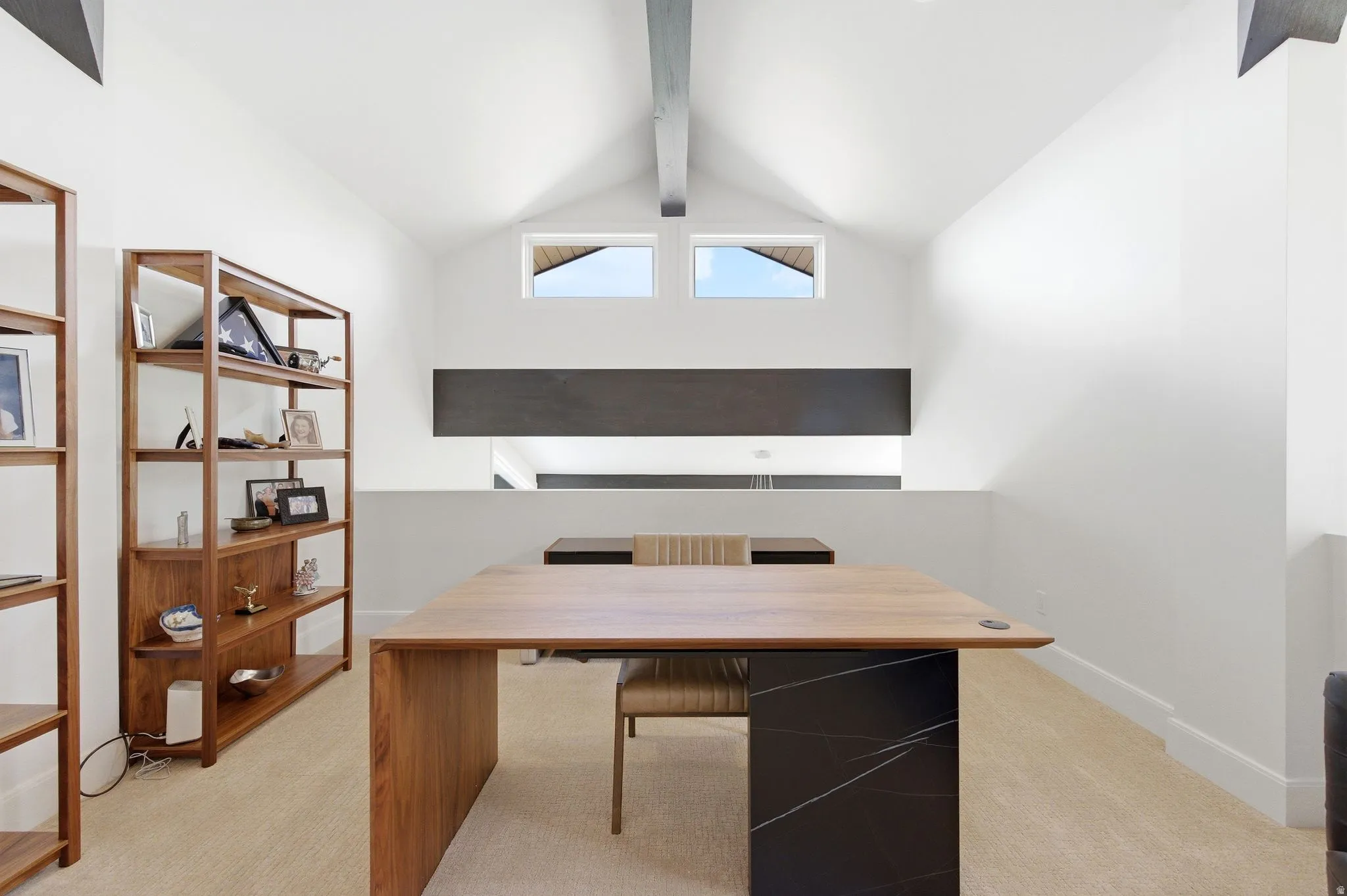 Loft space featuring a vaulted ceiling with exposed beam, dual clerestory windows, and architectural half-wall